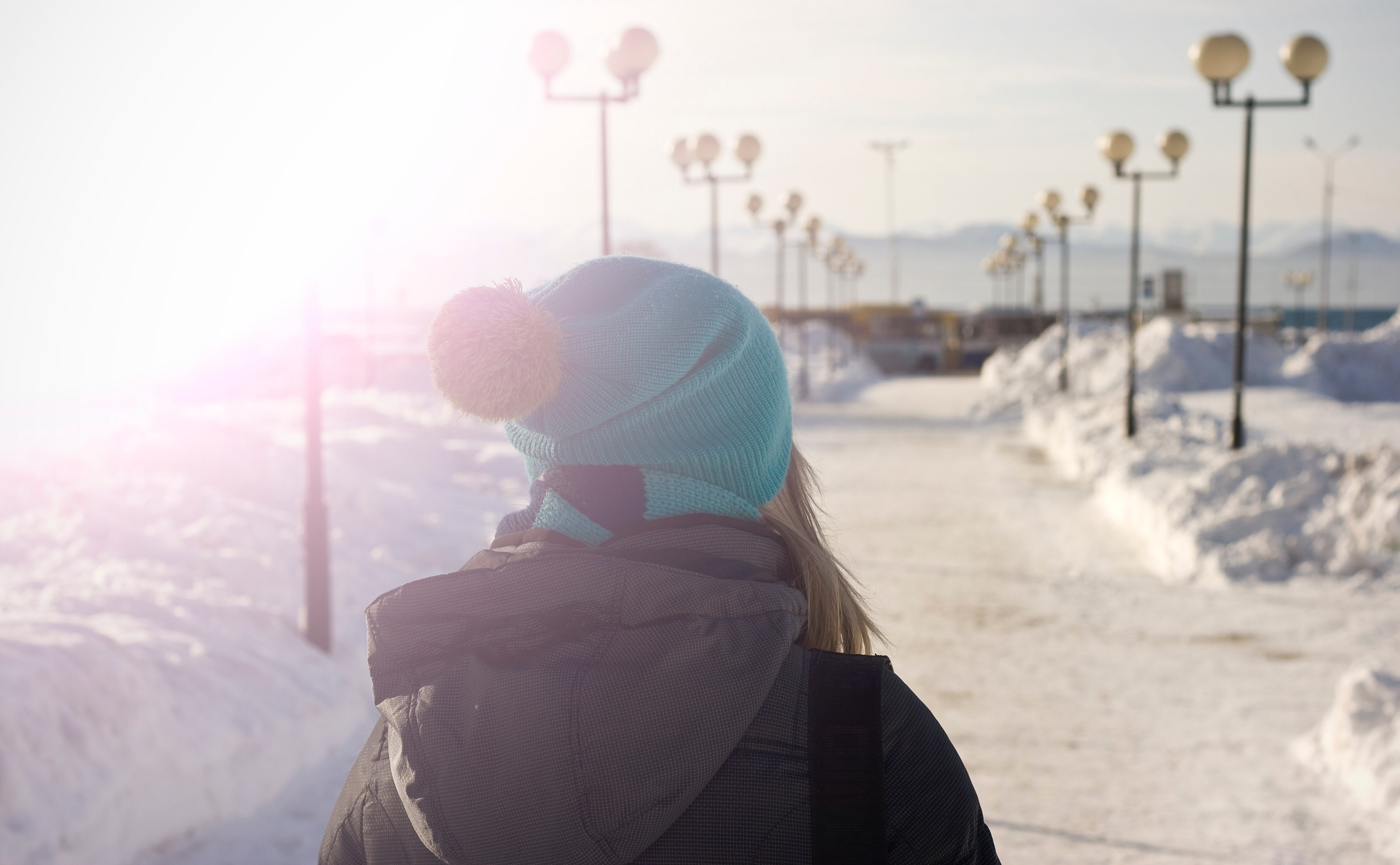 a female in a blue hat walking a snowy path of streetlights in the sun, a woman on a snowy street light path 4k, HD Wallpaper