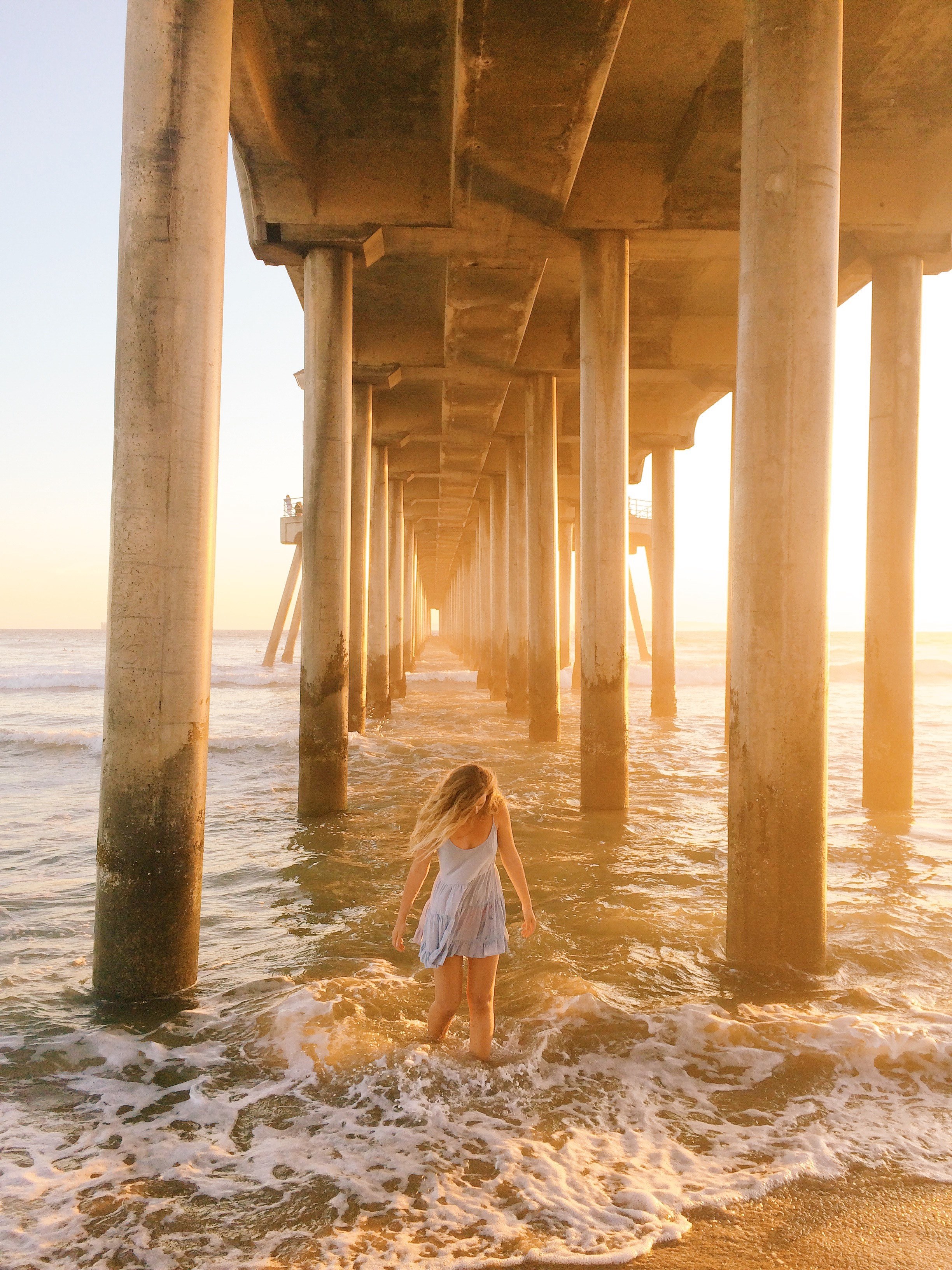 woman in shallow water between pier pillars at huntington beach, paddling beneath the boardwalk 4k, Phone HD Wallpaper