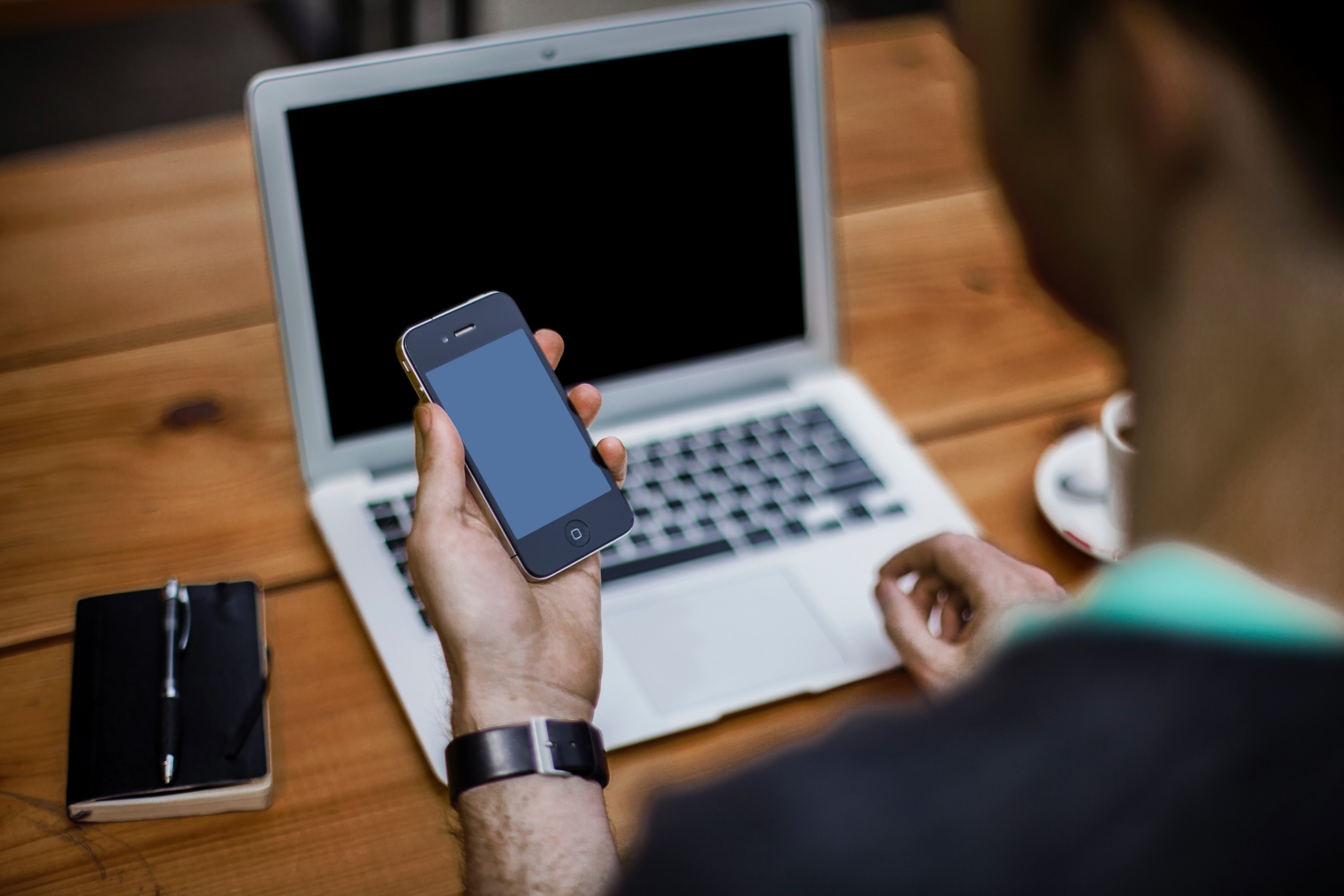 a man holding an iphone while sitting at a desk with a laptop, man with smartphone and laptop 4k, HD Wallpaper