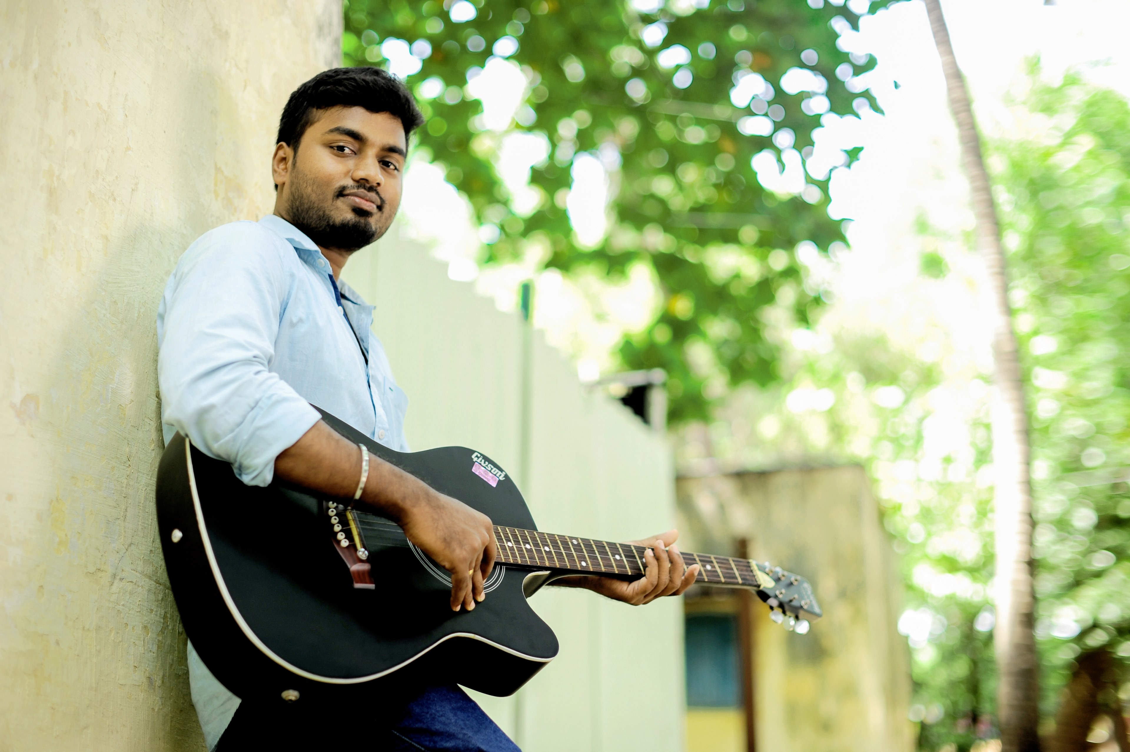 a man with a black guitar leaning against the wall on a bright day, acoustic guitar player in chennai 4k, HD Wallpaper