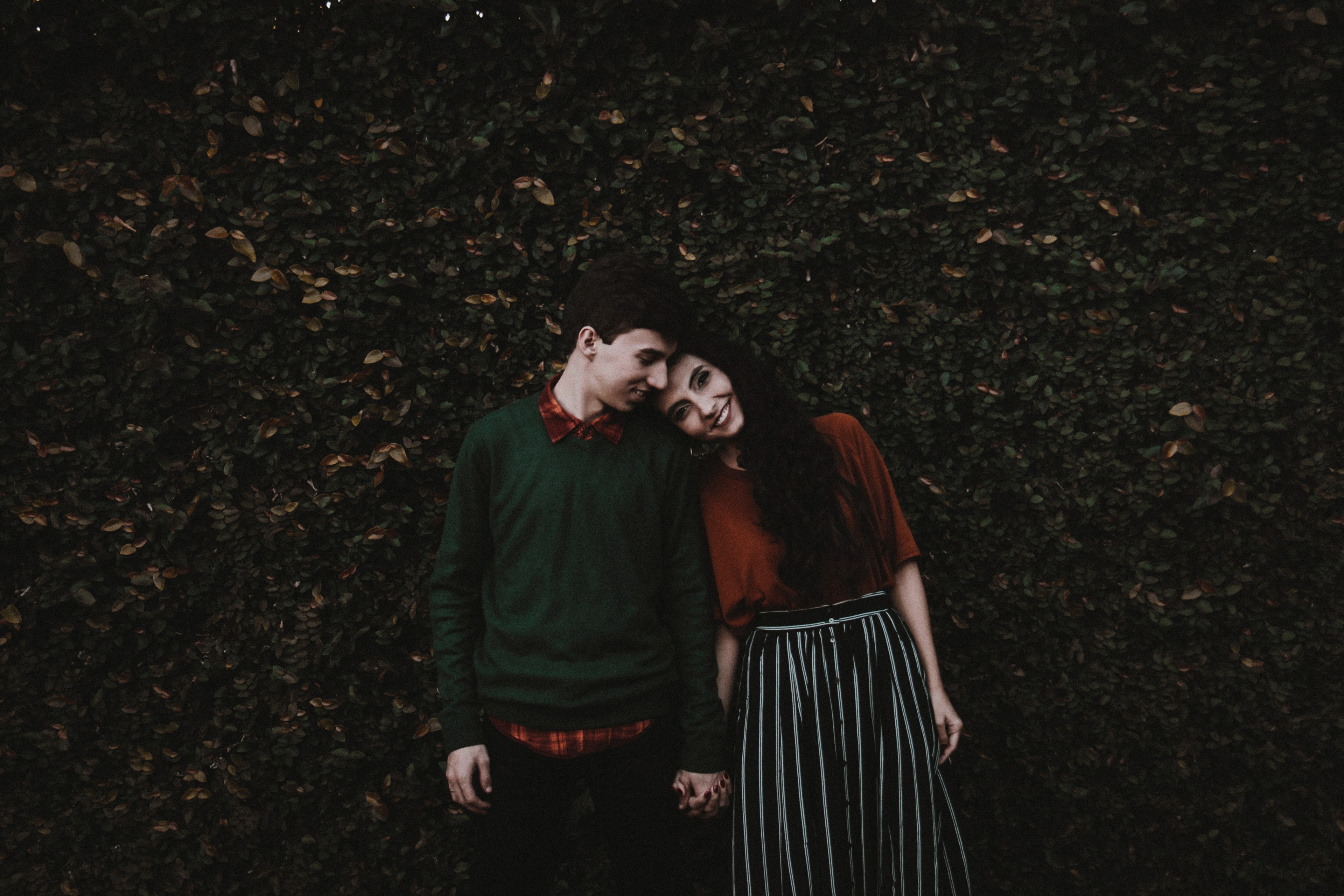 couple holds hands and leans their heads together in front of a leafy wall in cianorte, leaning together in cianorte 4k, HD Wallpaper