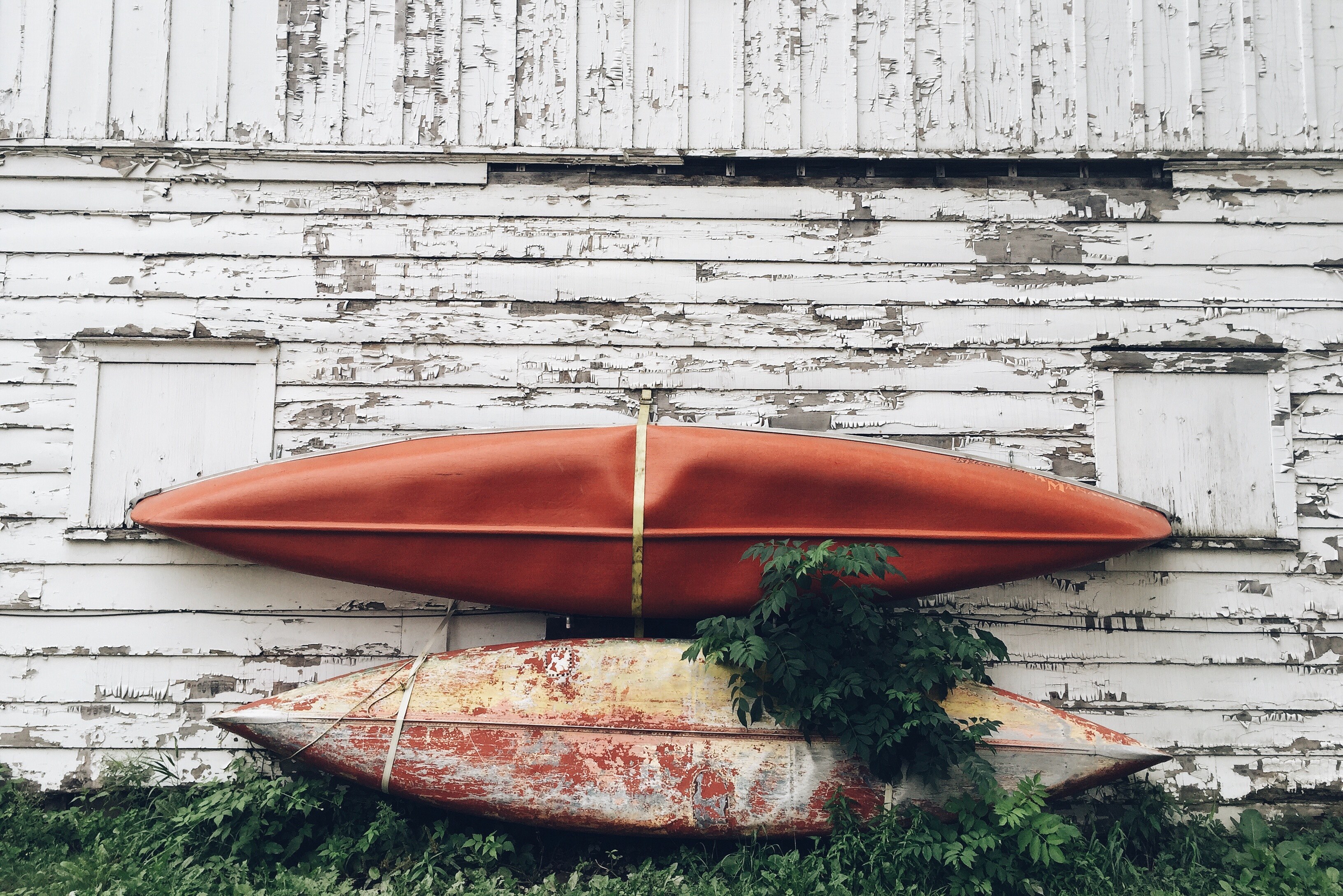 two used kayaks leaning on an old barn wall with peeling white paint and unkept grass, _two kayaks leaning on a wall 4k, HD Wallpaper