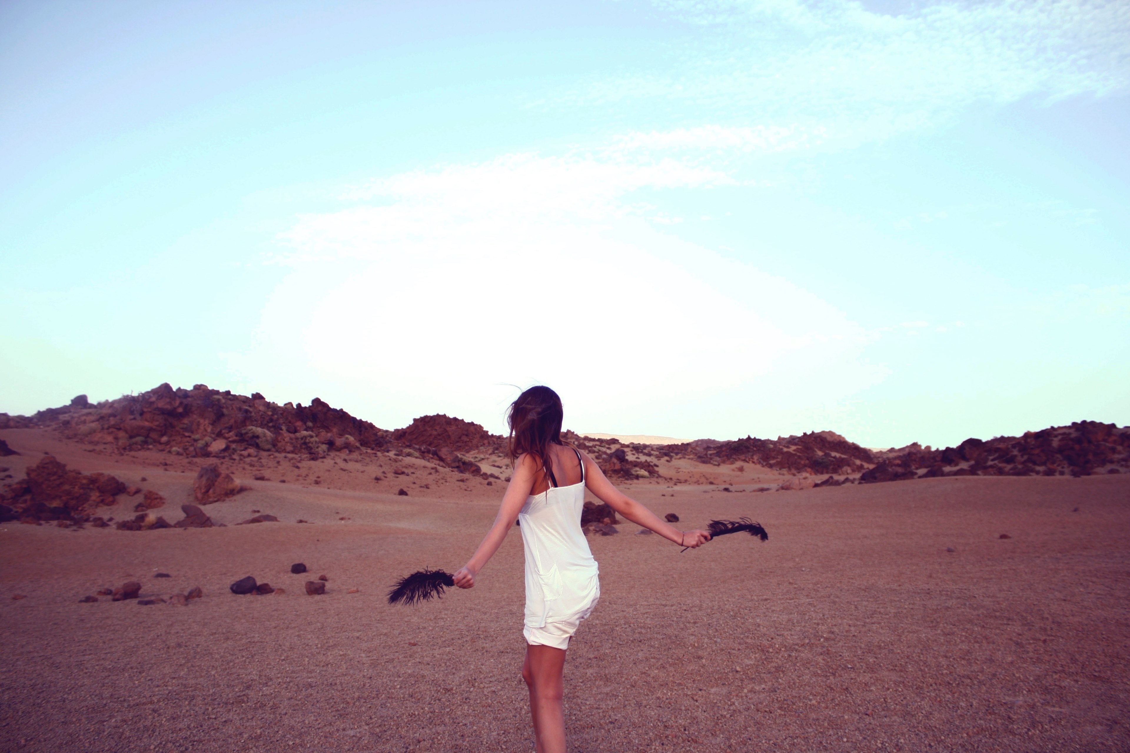 a carefree young woman with a black feather in either hand in the middle of a barren rocky plain, dancing in a rocky plain 4k, HD Wallpaper