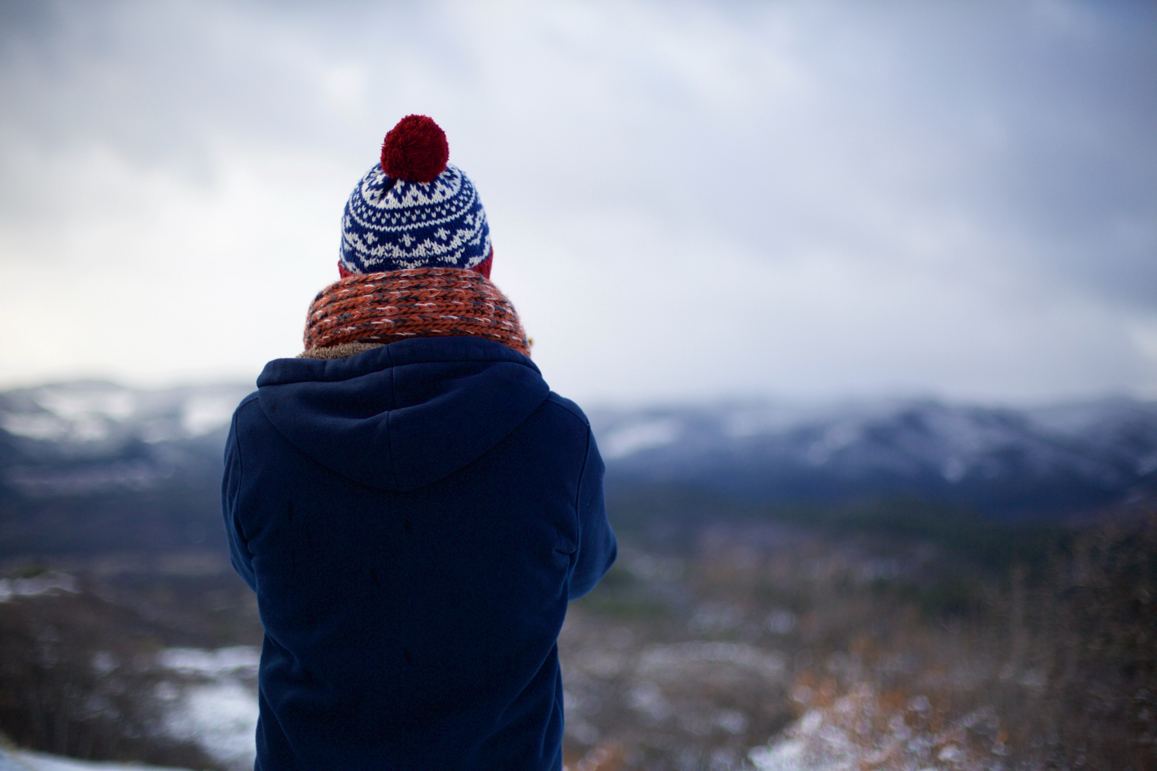 the back of a person with crossed arms wearing a knit cap scarf and blue coat is visible as he or she stares out into snowy wilderness, person stares into wilderness 4k, HD Wallpaper