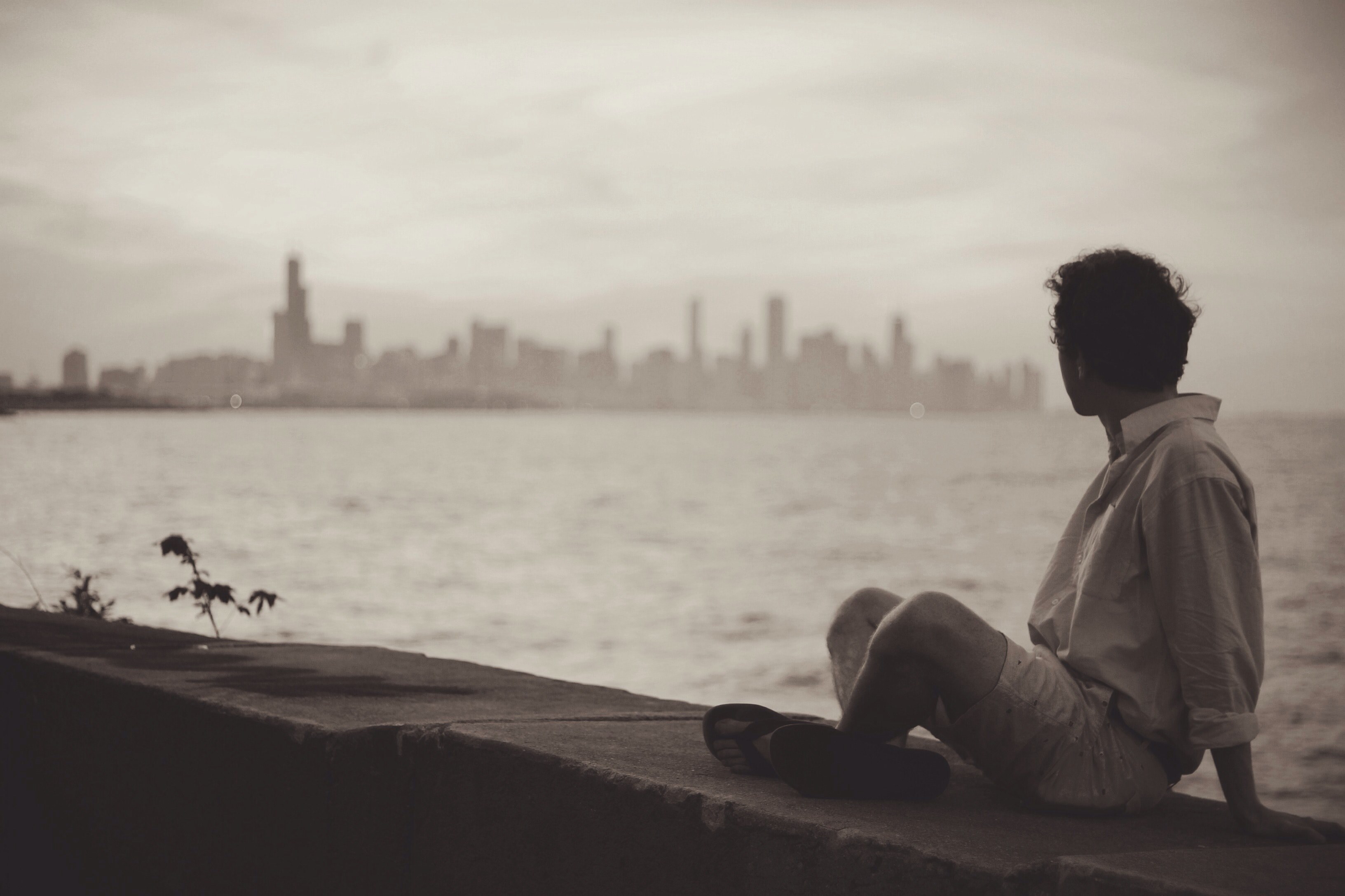 man sitting on stone wall in front of water and city skyline, man in front of skyline 4k, HD Wallpaper