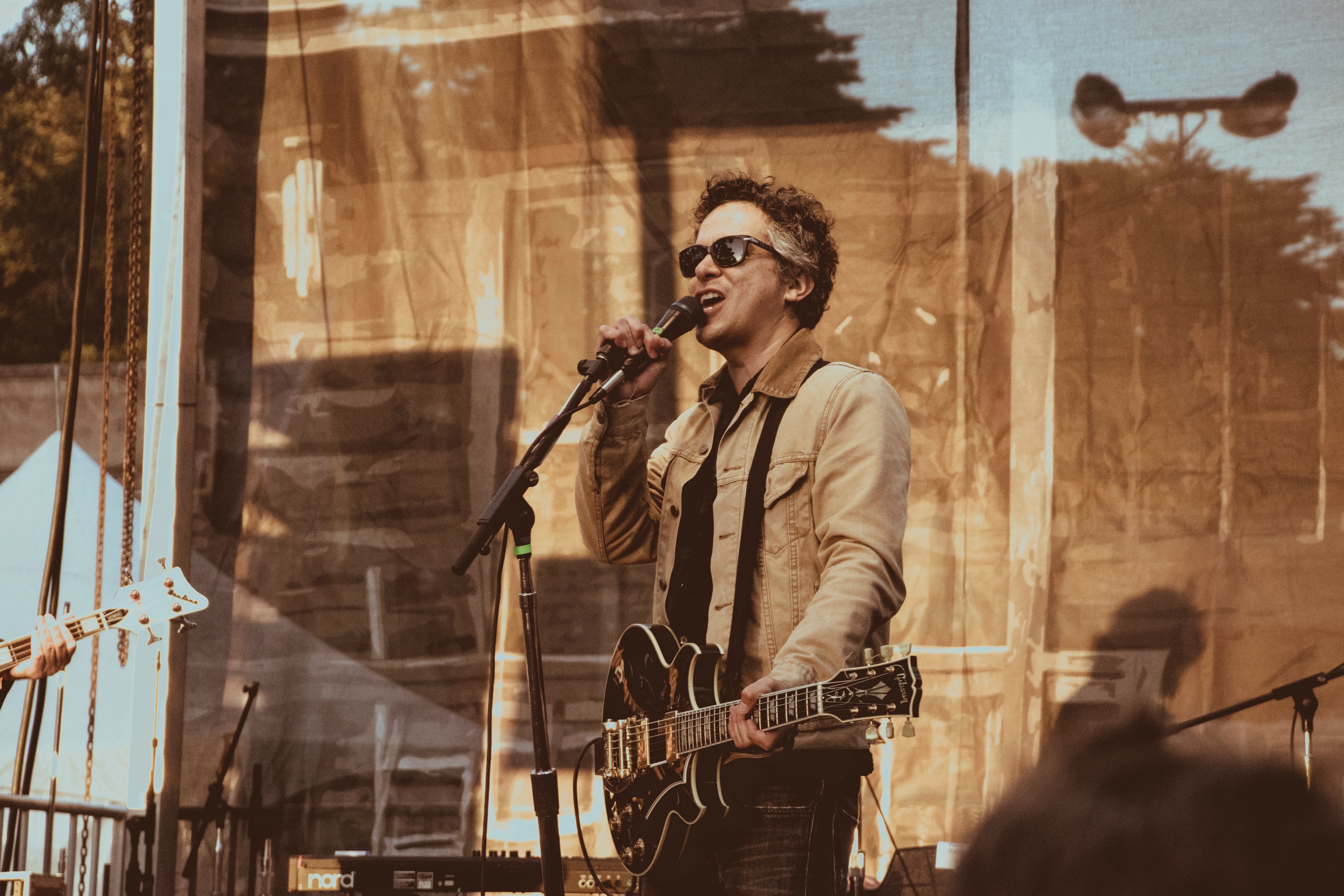 a man in sunglasses holding an electric guitar and speaking into a microphone on stage, band member introducing a song 4k, HD Wallpaper