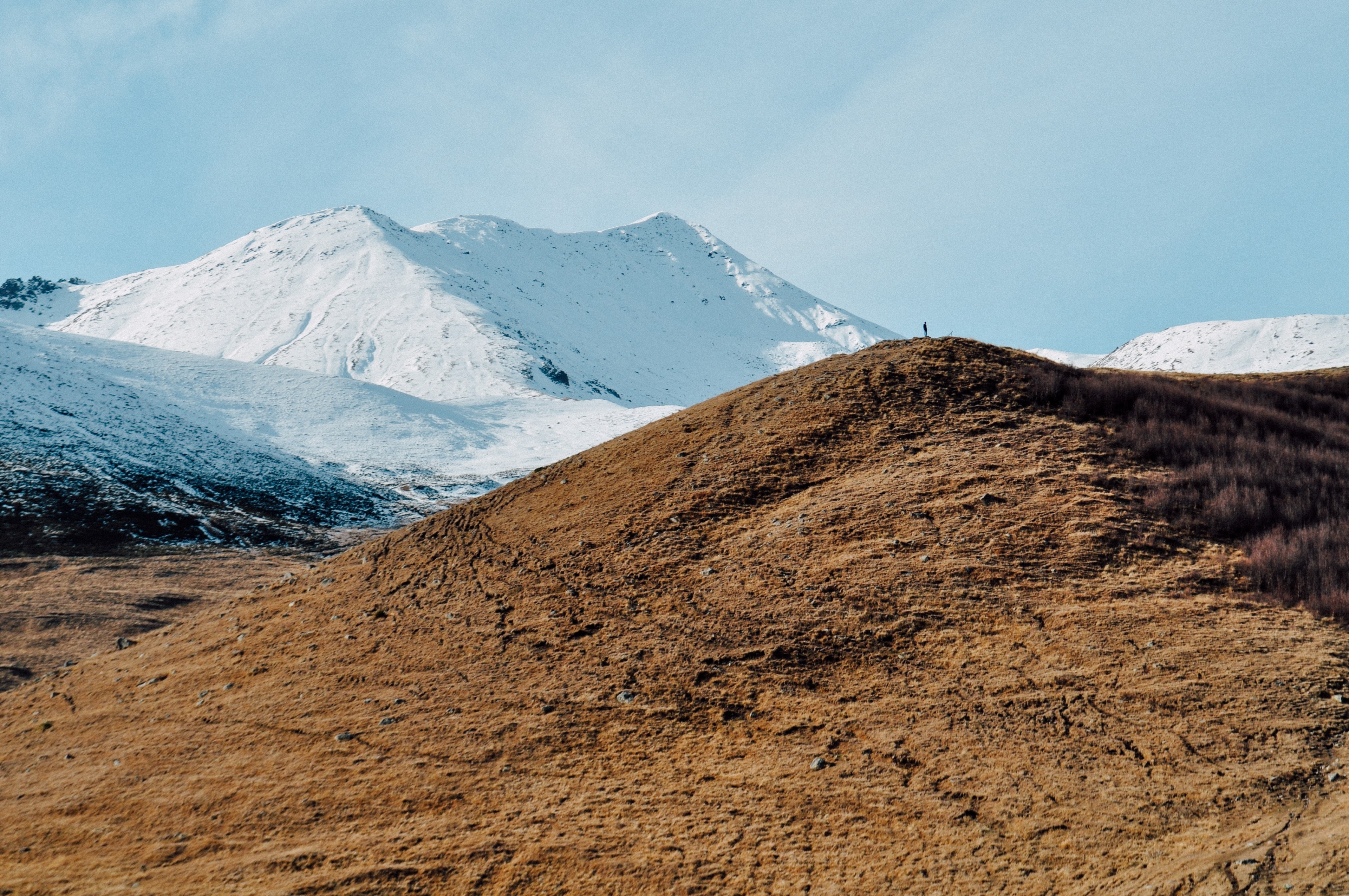 a giant dry and rocky mound in front of a backdrop of snowy mountains, rocky and snowy mountains 4k, HD Wallpaper