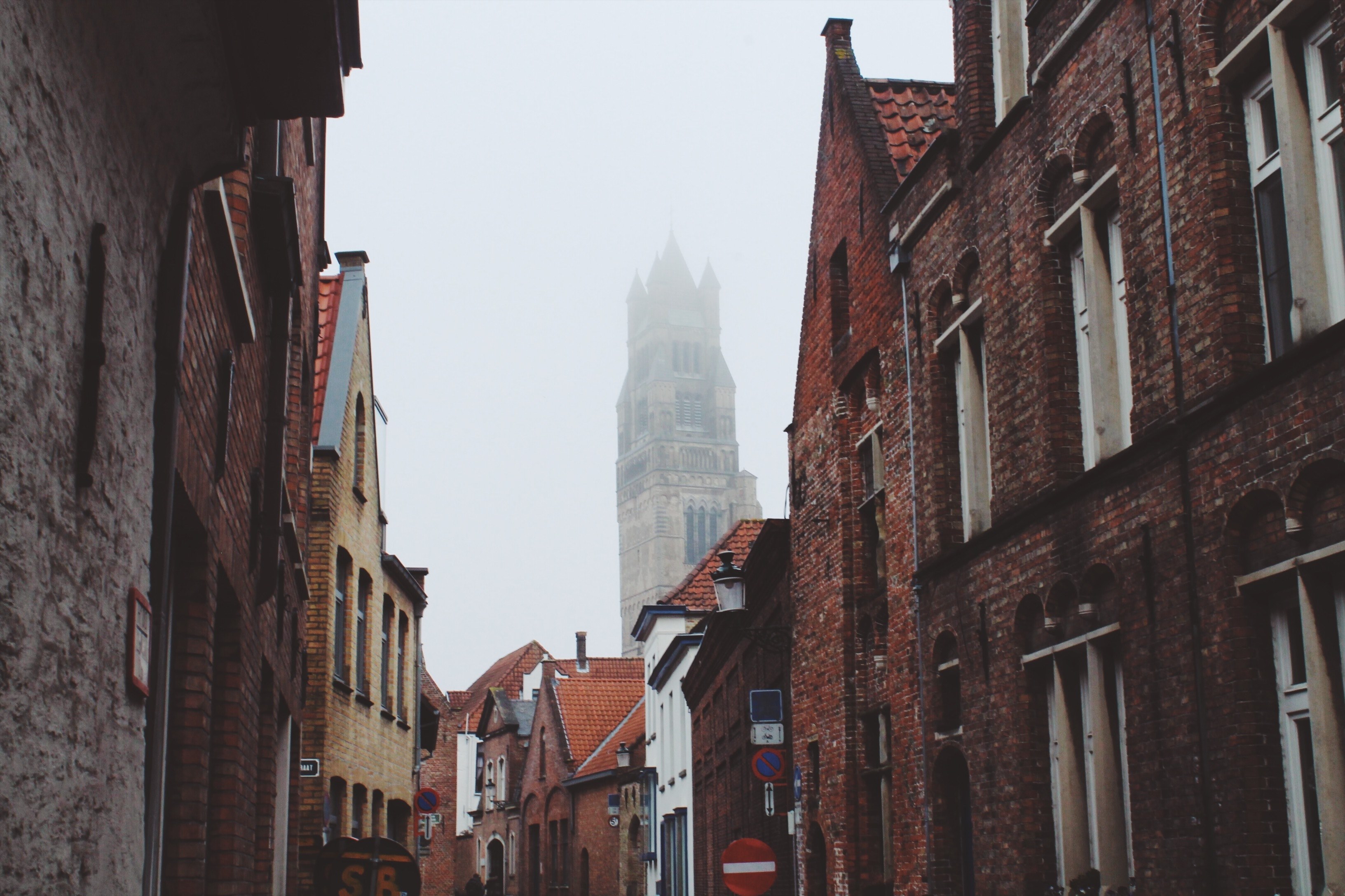 a street in bruges with brick houses and a church covered in fog in the background, foggy day in brugge 4k, HD Wallpaper