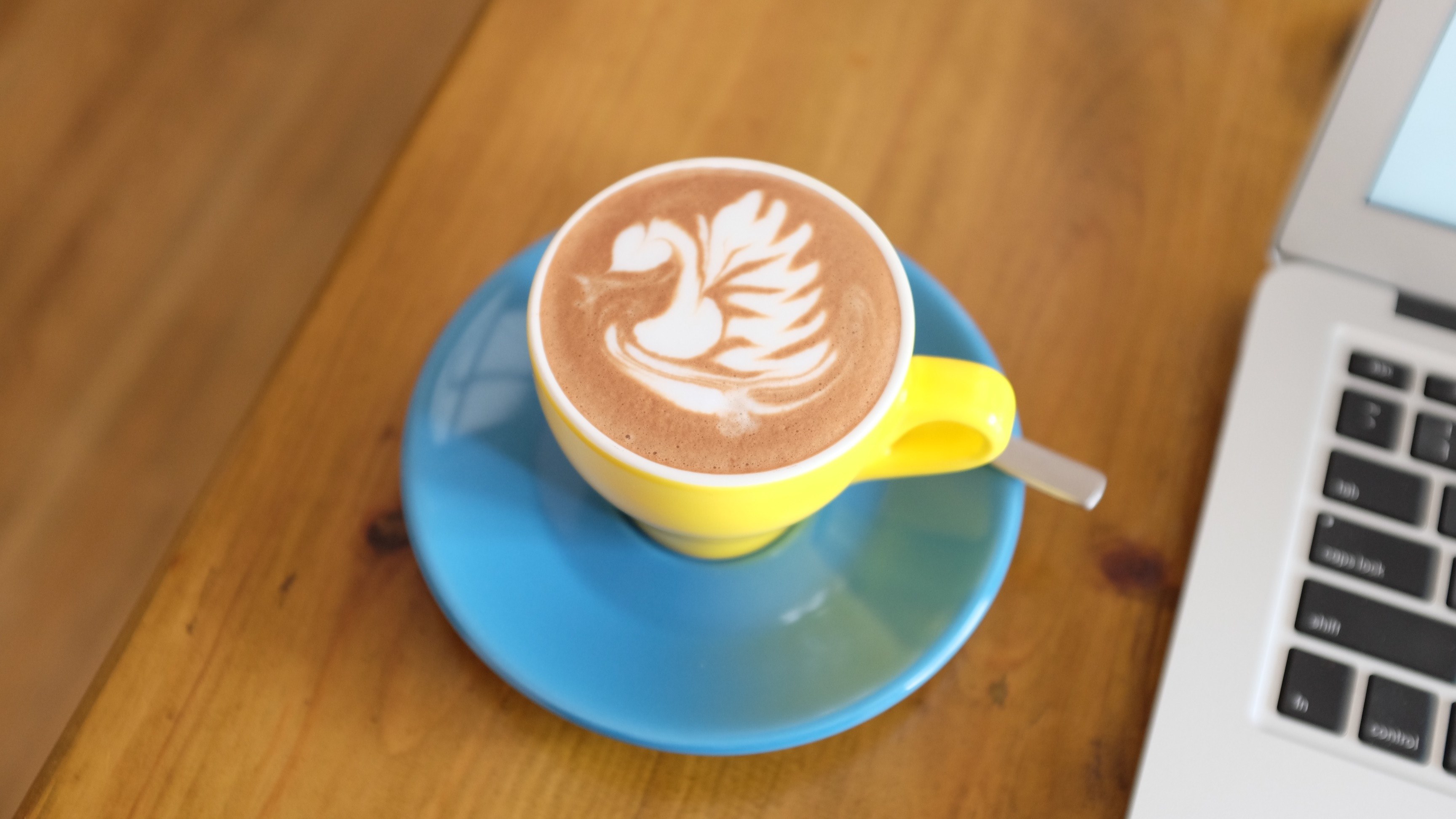 a yellow cup with latte art on a blue saucer next to a macbook, latte art and laptop 4k, HD Wallpaper
