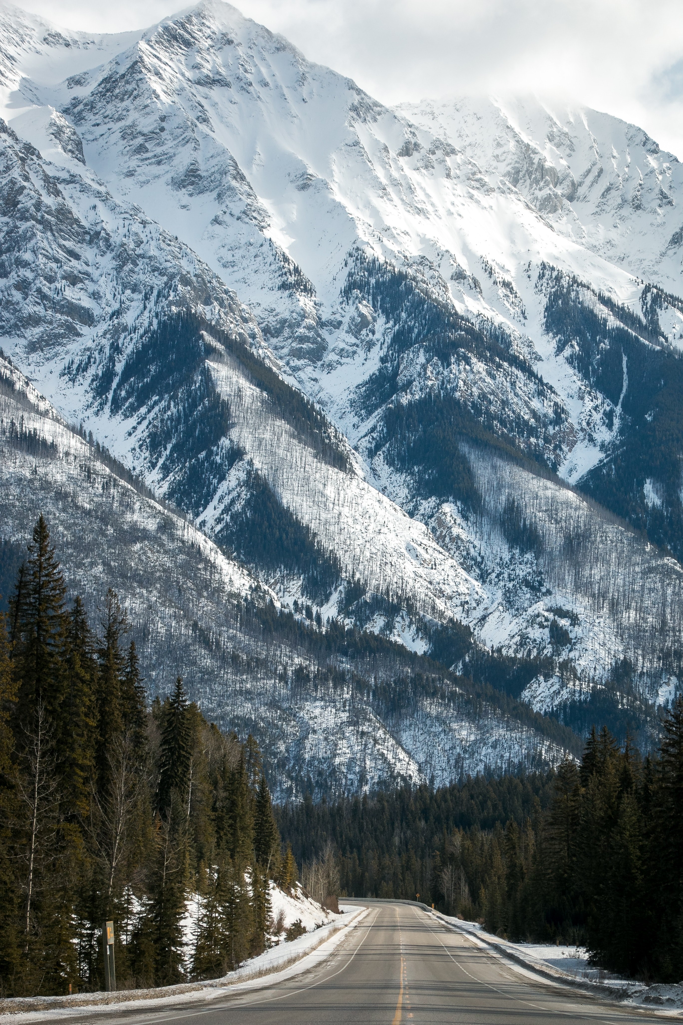 an empty asphalt road along a tall snow covered mountain in the canadian rockies, beneath the giants 4k, Phone HD Wallpaper