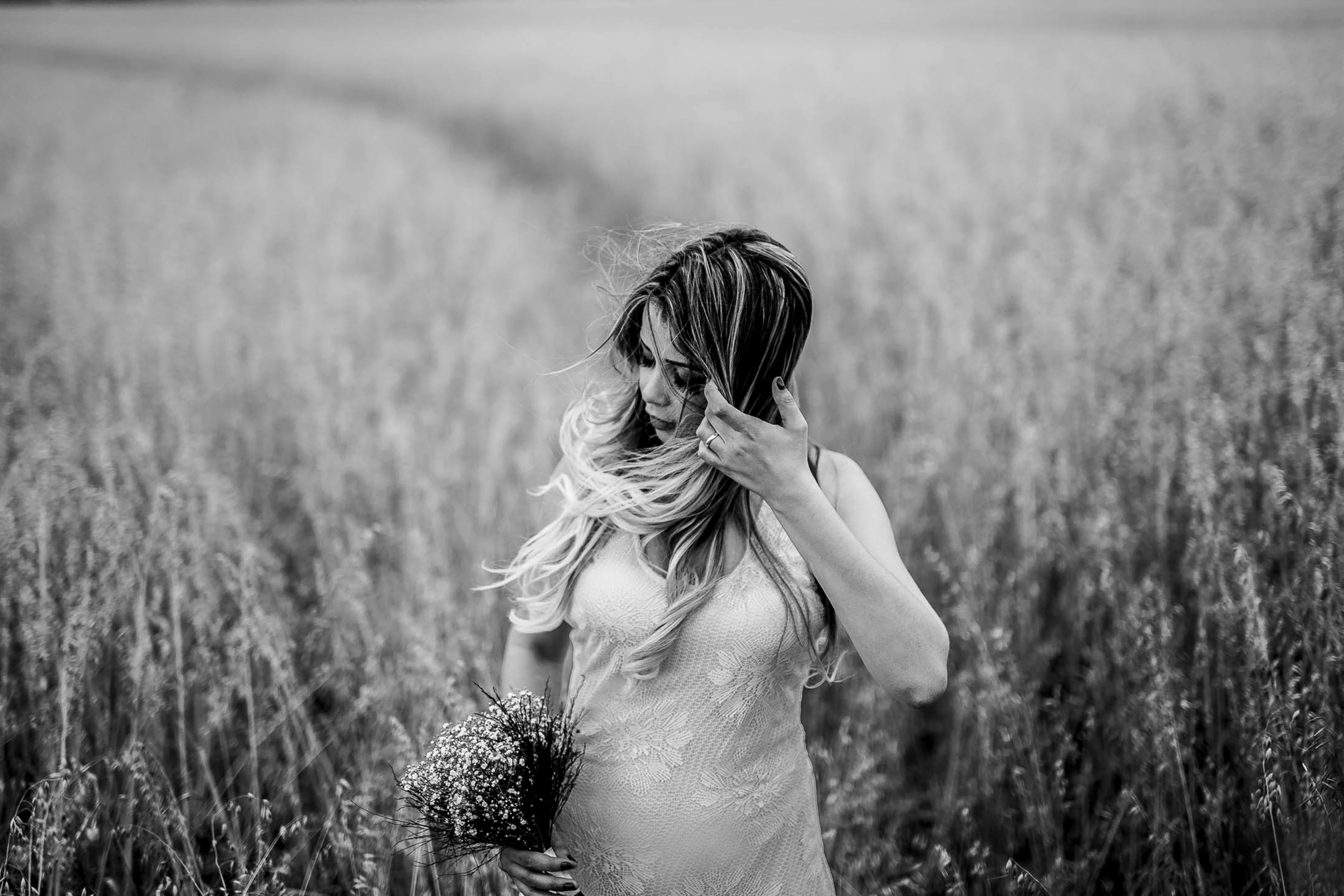 a black and white shot of a woman with a floral bouquet brushing back her hair in a field, woman in a field in monochrome 4k, HD Wallpaper