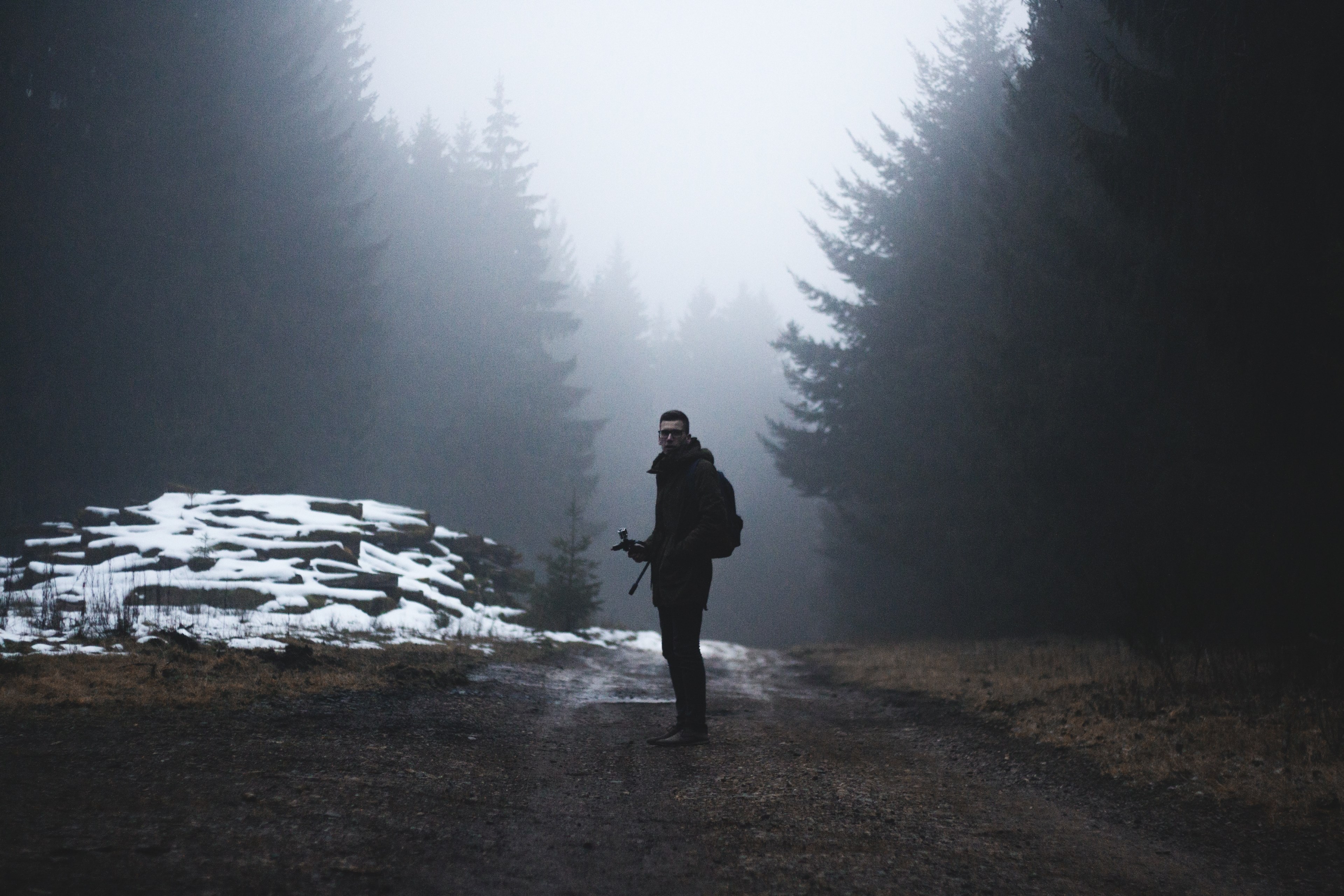 man stands on a path surrounded by evergreen trees and slight dusting of snow, man standing on dirt path 4k, HD Wallpaper