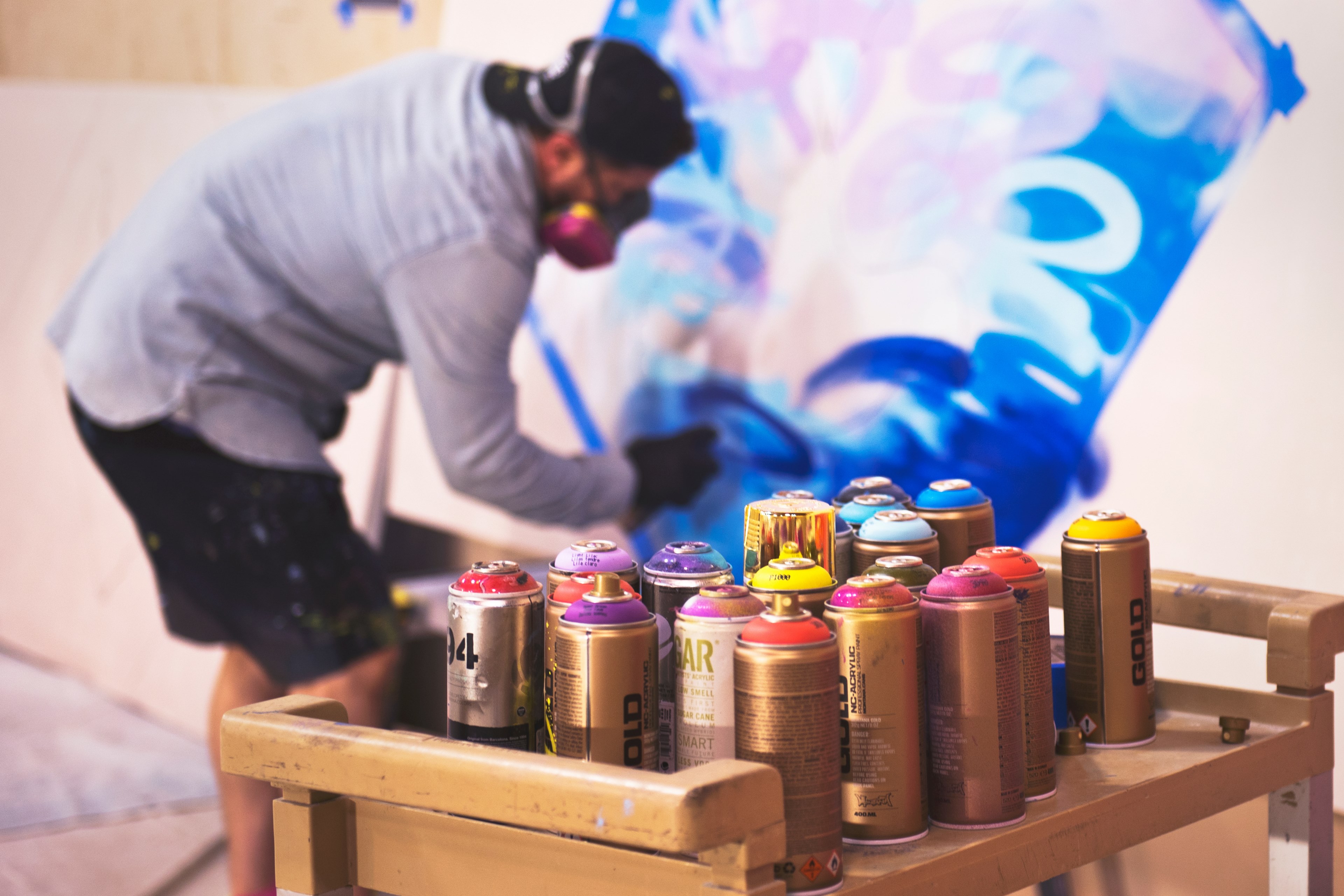 a rack with spray cans near a man painting blue graffiti art on a wall, sprayed 4k, HD Wallpaper