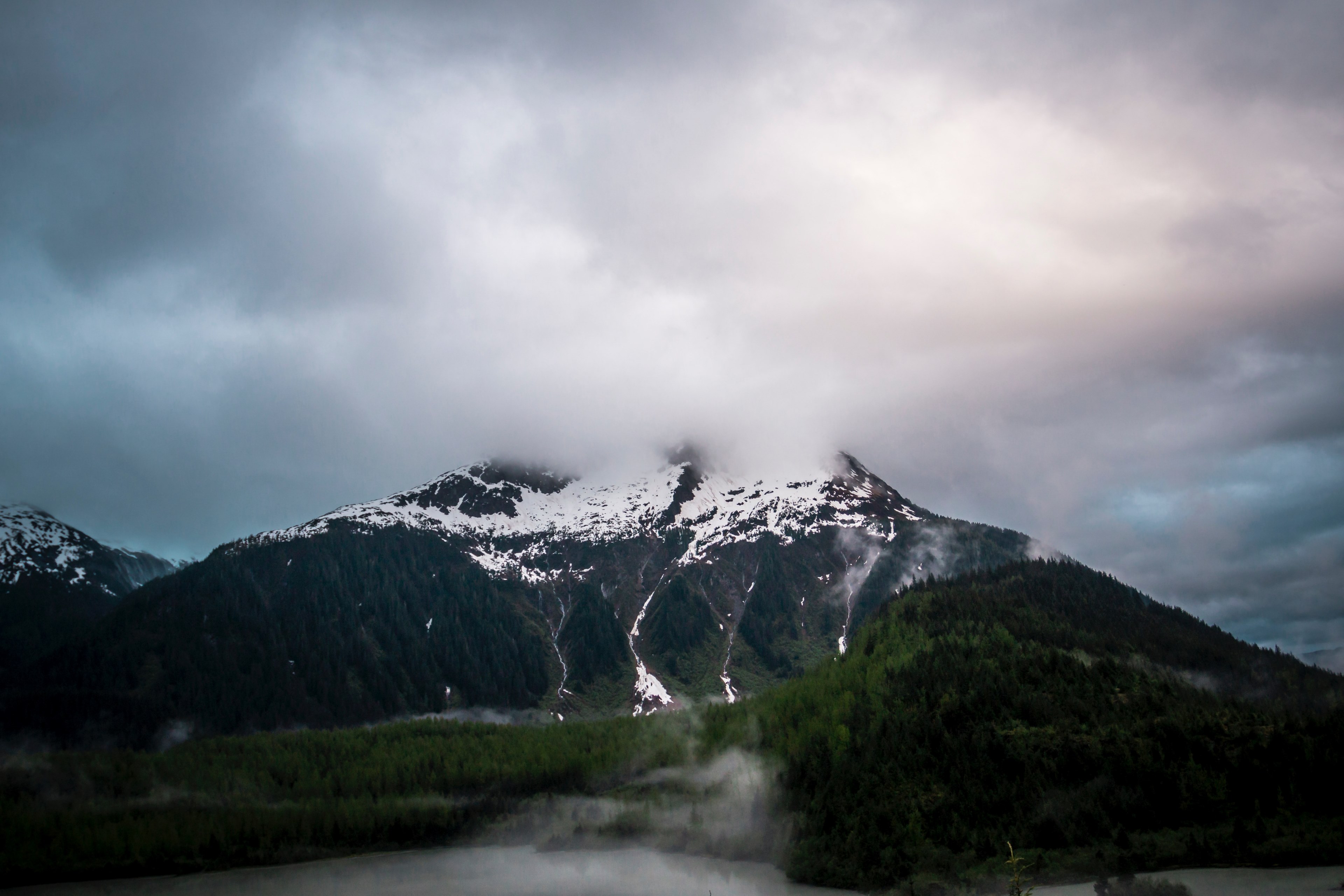 a tall mountain by a lake with its peak shrouded by dense clouds, misty tips 4k, HD Wallpaper