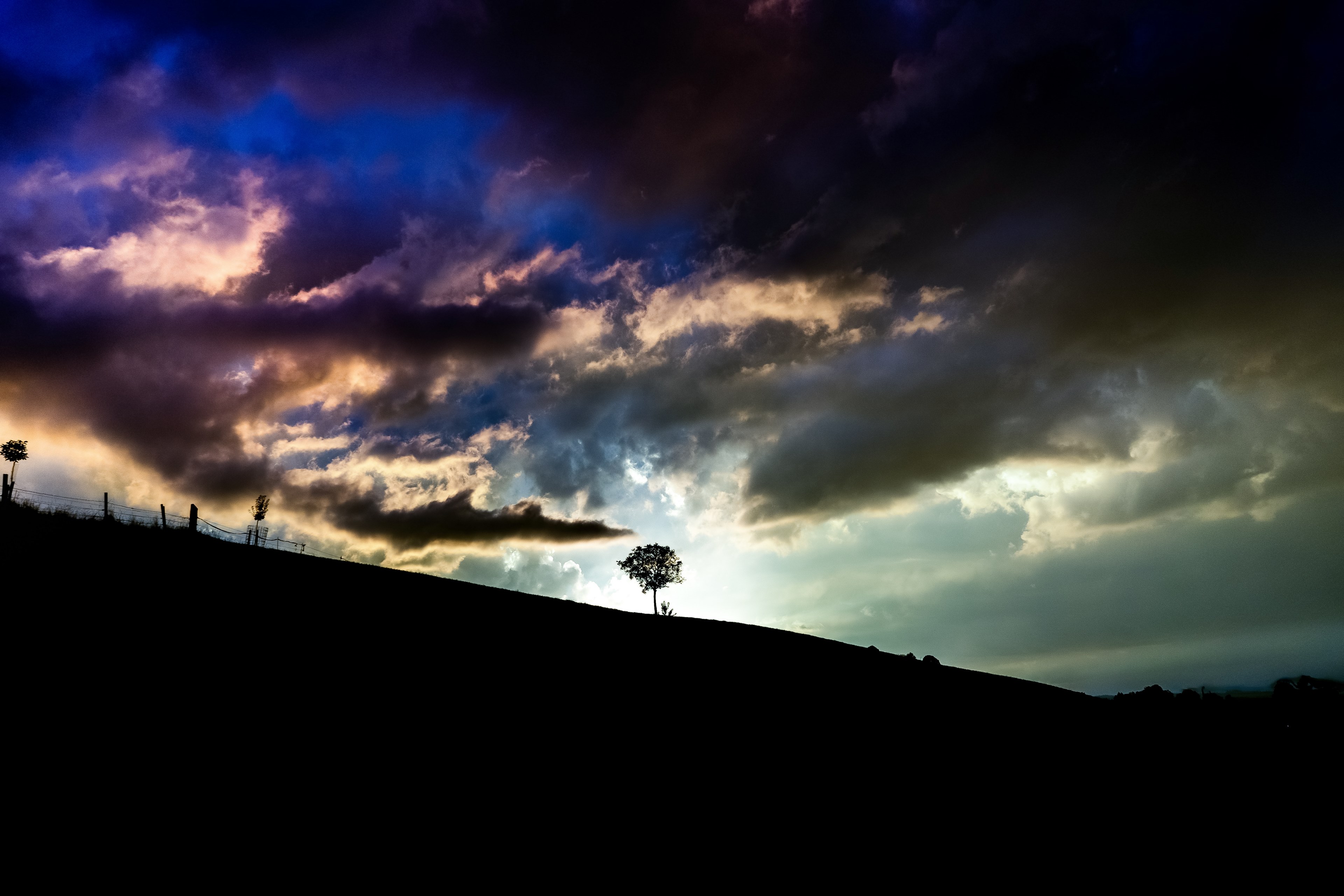 a dark sunset in the horizon casts shadows on a hill where some trees and fences stand in hfen, dark sunset at hfen 4k, HD Wallpaper