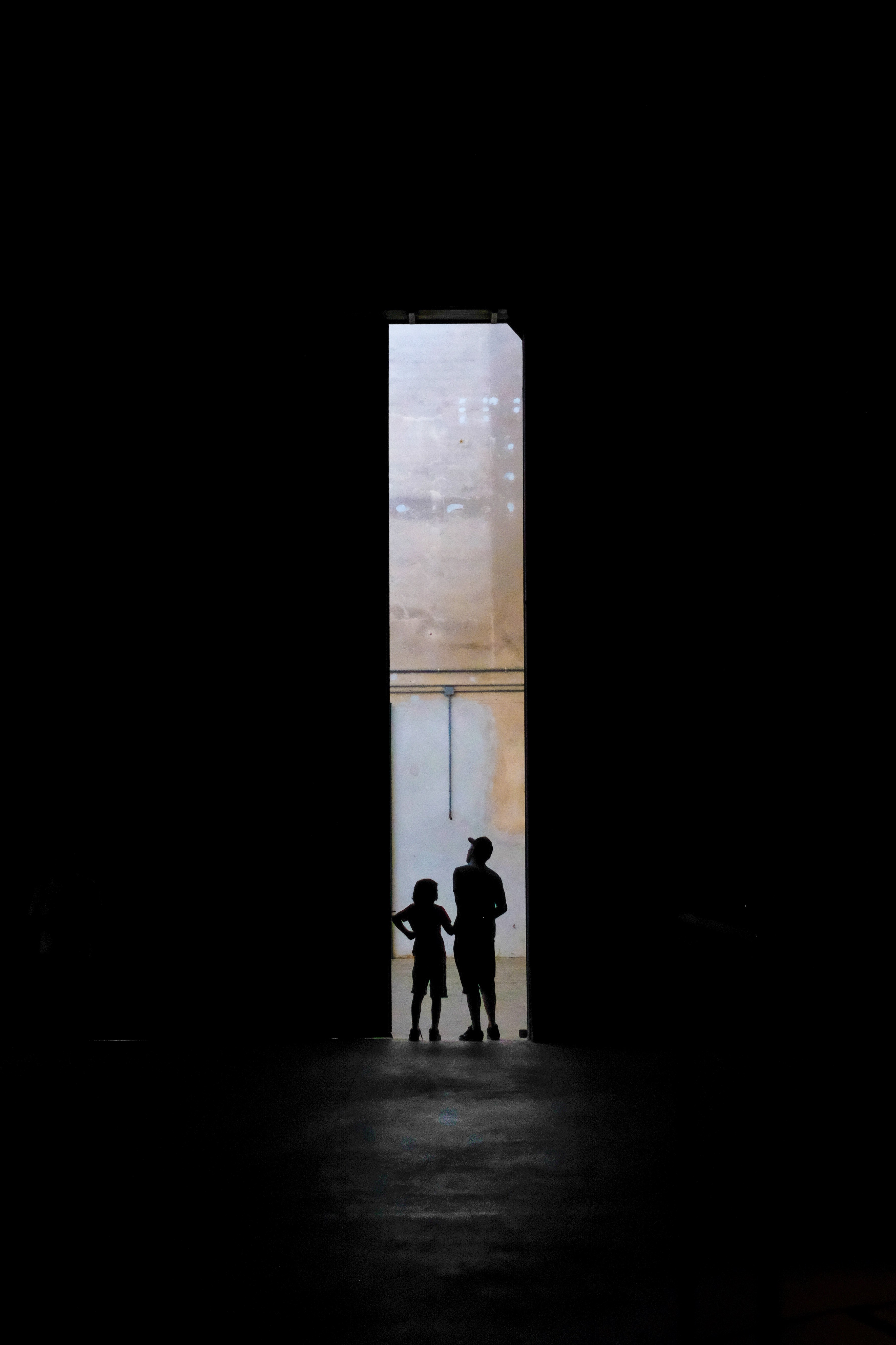 two kids stand silhouetted against the far opening of a narrow tall dark passageway, the passage beyond 4k, Phone HD Wallpaper