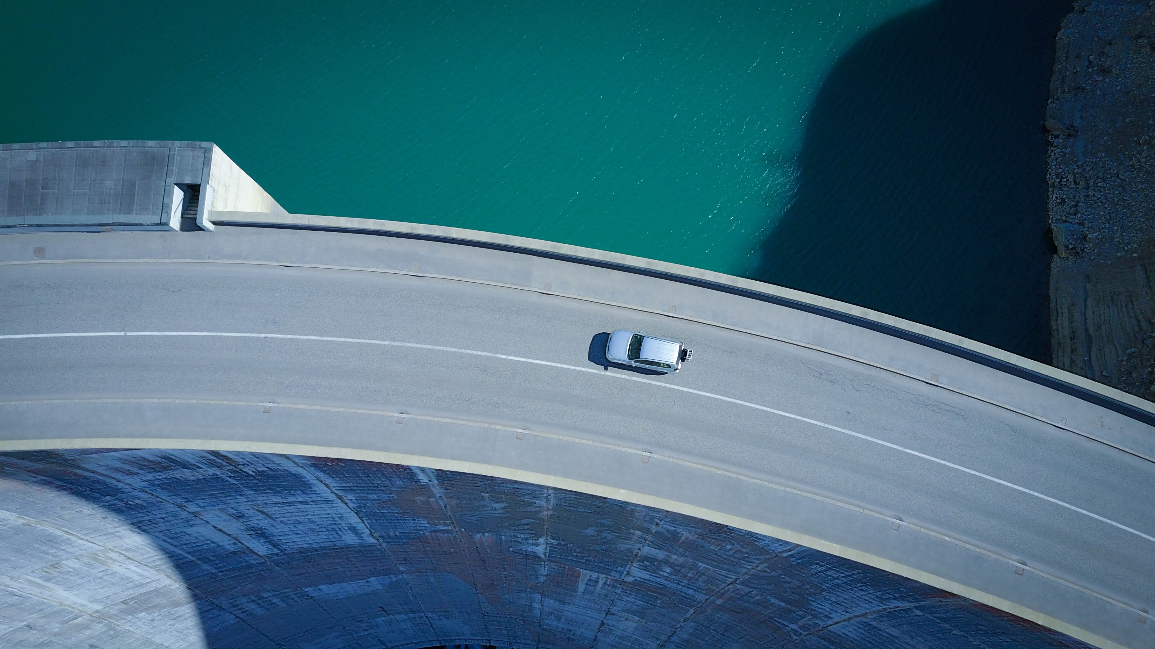 an aerial shot of a car driving along a curve in a road on a tall dam, on the high road 4k, HD Wallpaper