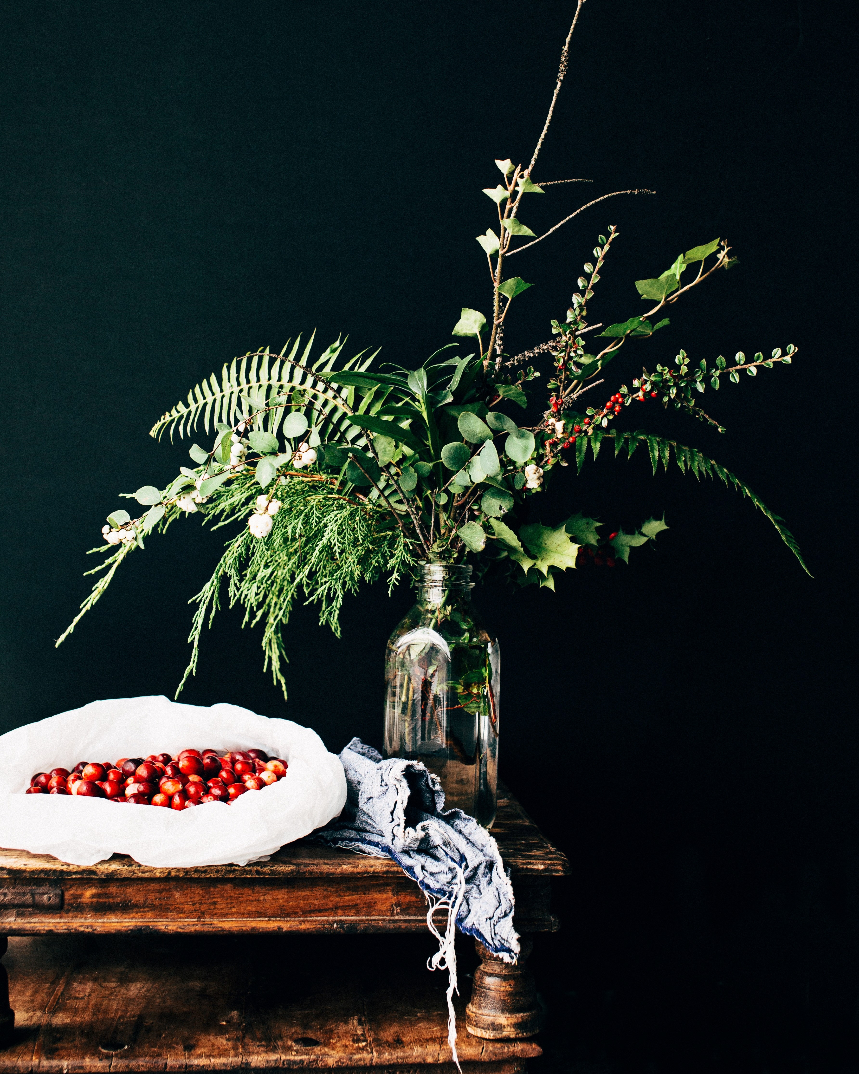 a wooden table with a sack of berries and a glass vase with different types of green plants in it on top, holiday arrangement 4k, Phone HD Wallpaper