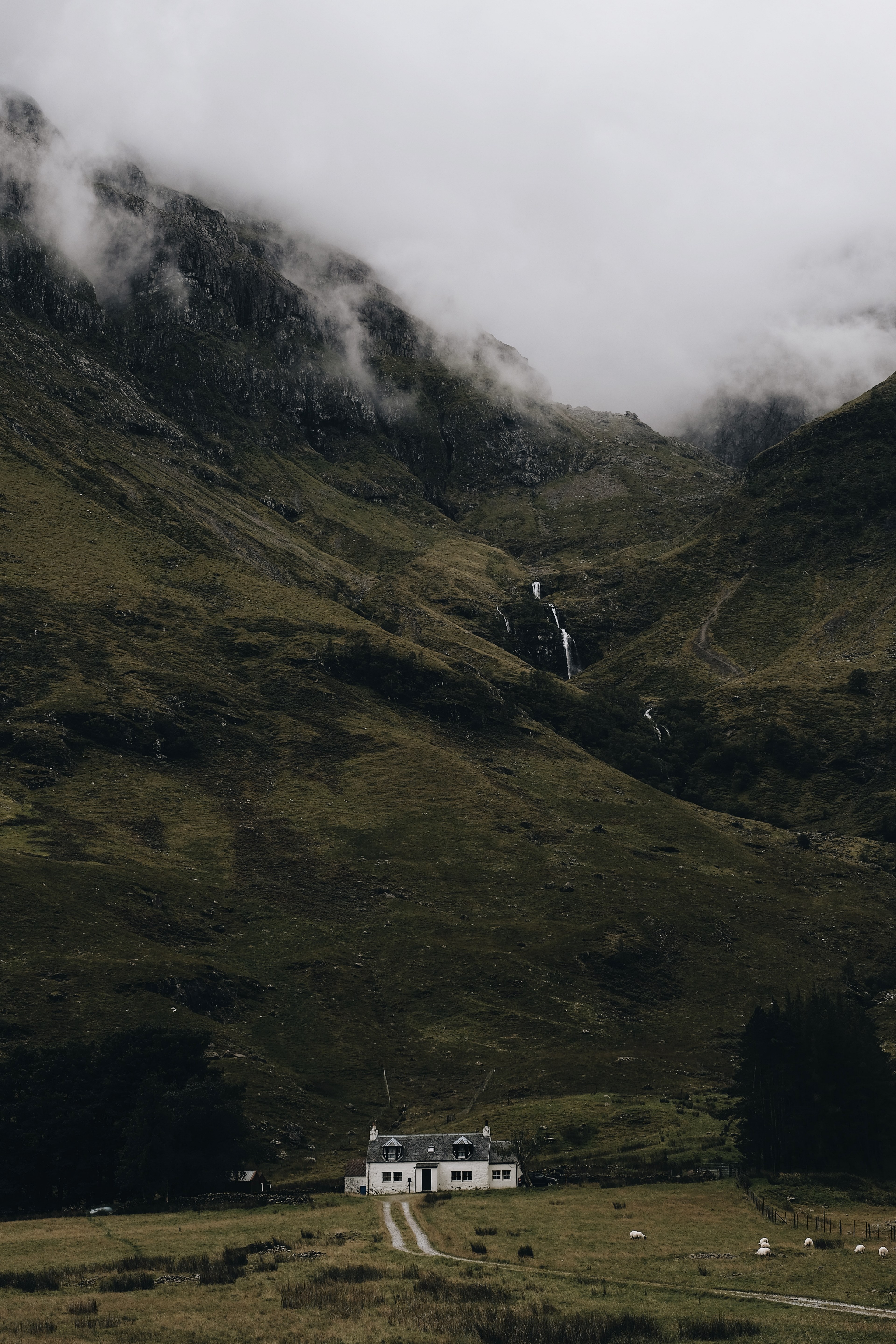 house at the base of a mountain with clouds and a waterfall on the rocks of the mountain, the lonely house 4k, Phone HD Wallpaper