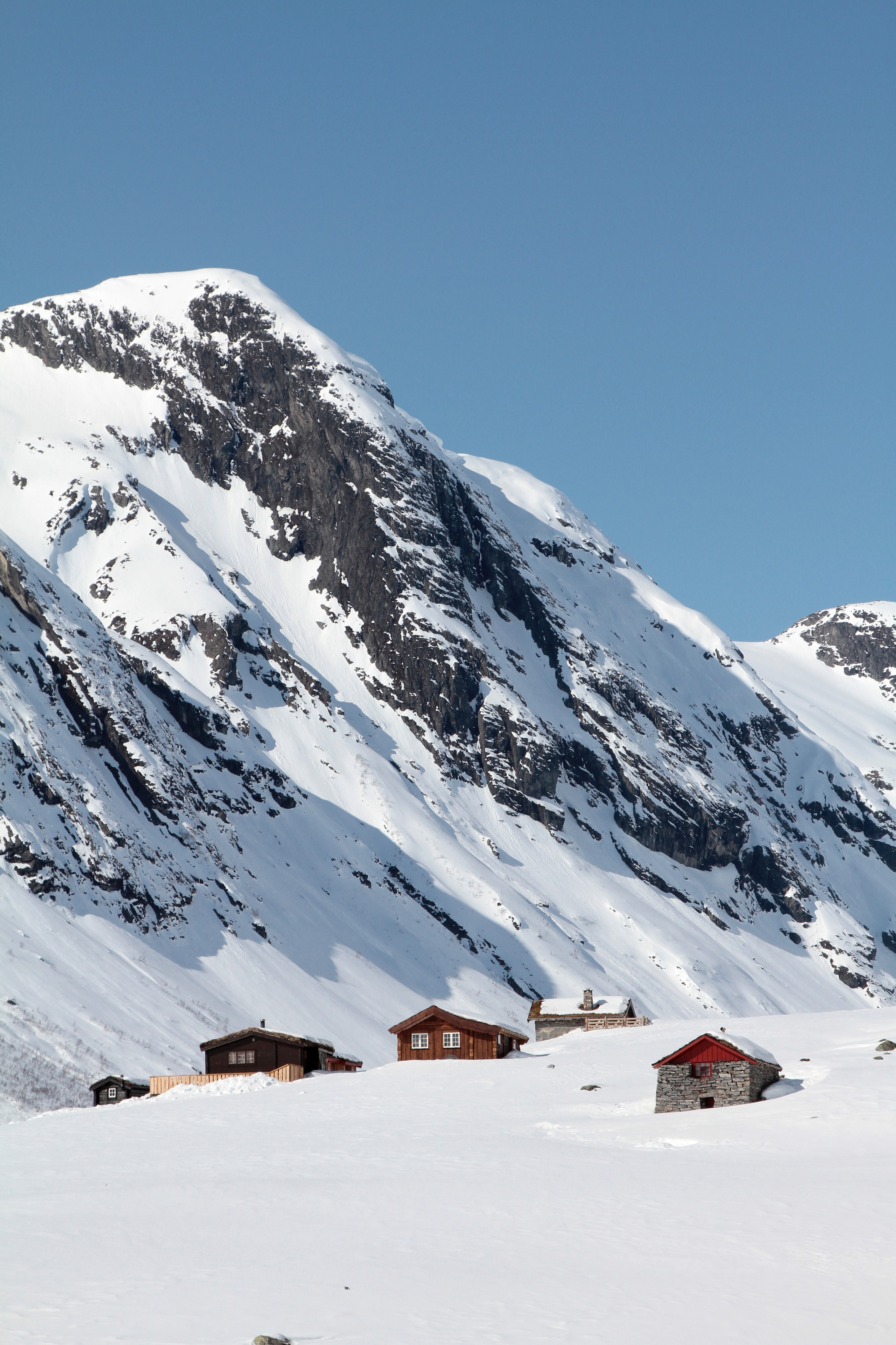 houses at the top of a hill with snow capped mountains in the background and blue skies, strynefjellets snowy cabins 4k, Phone HD Wallpaper