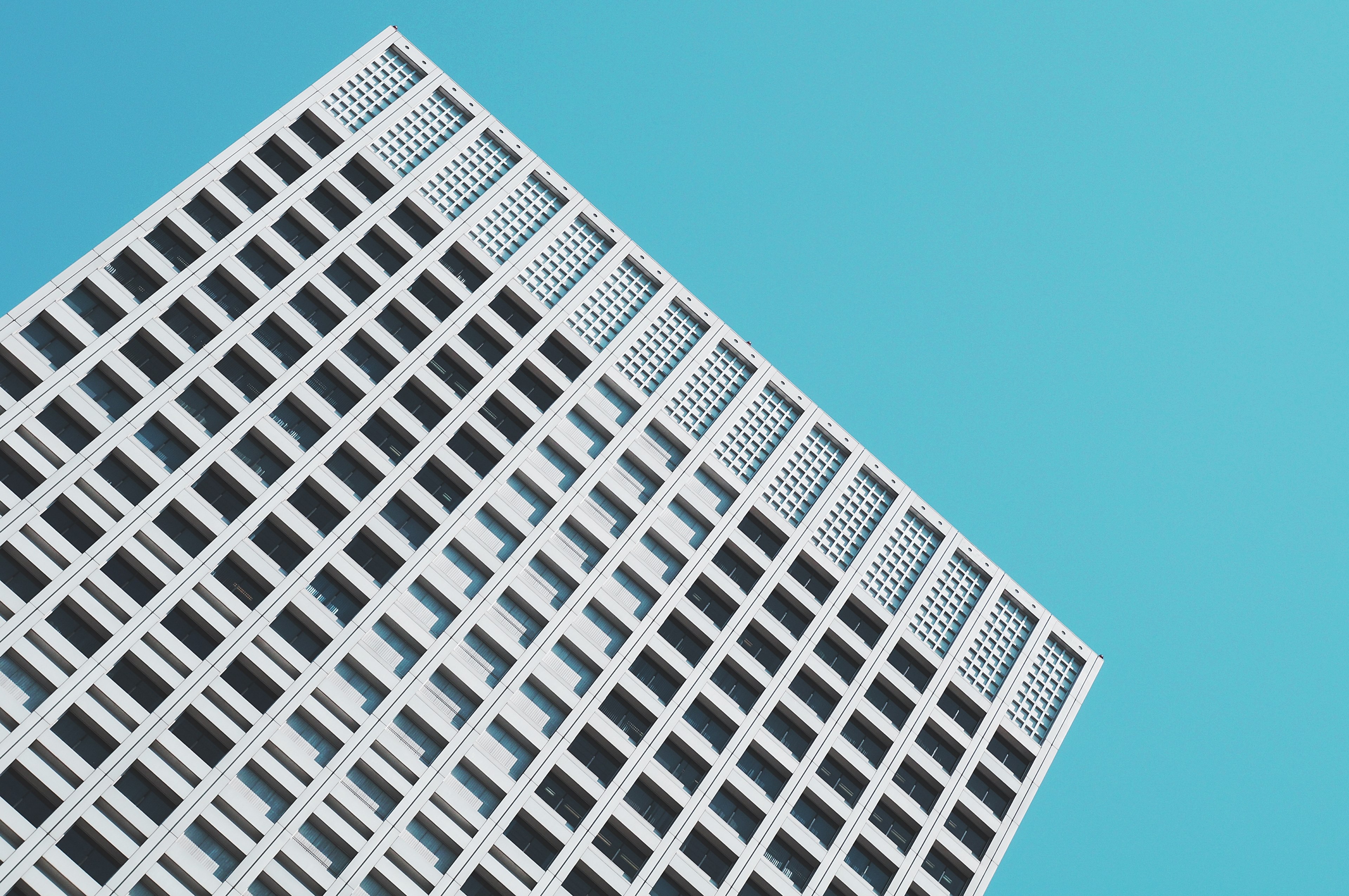 a minimalist concrete skyscraper building with many windows stands at an angle under blue sky, concrete building at angle 4k, HD Wallpaper