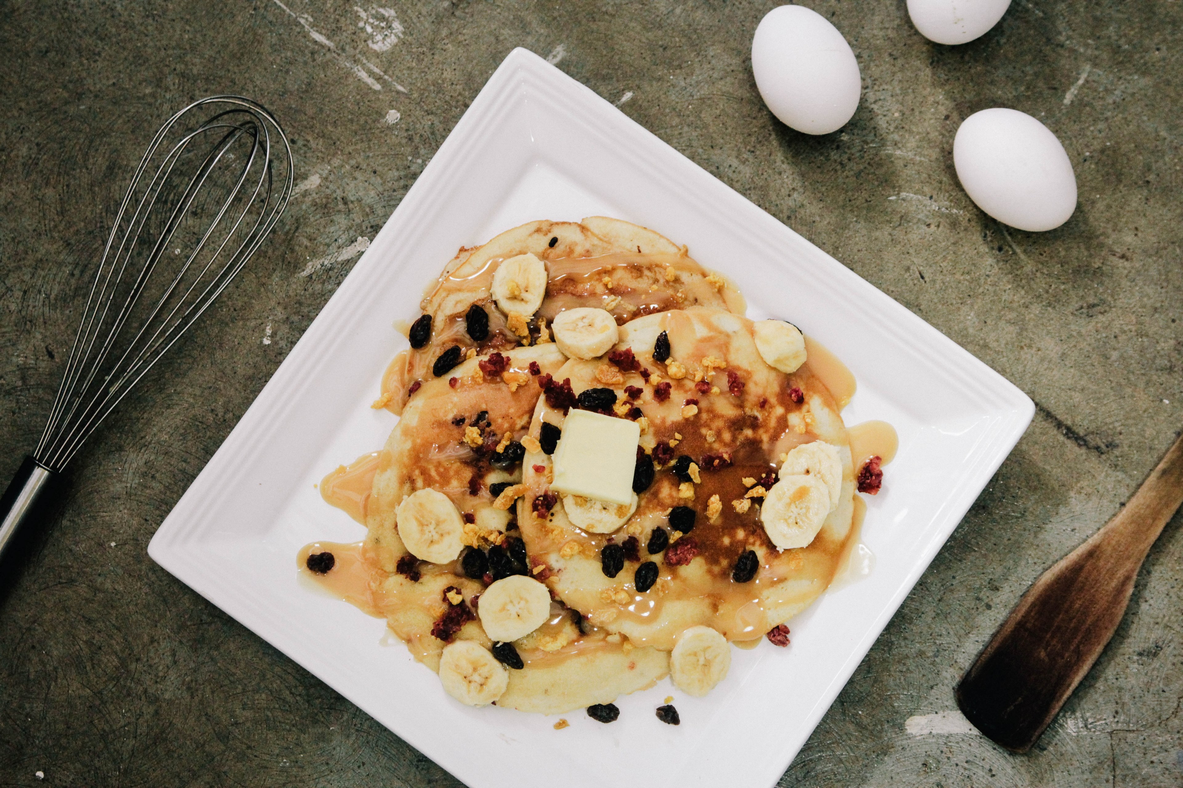 banana pancakes with raisins and syrup on a white plate eggs and cooking utensils on a countertop in makati, homemade banana pancakes 4k, HD Wallpaper