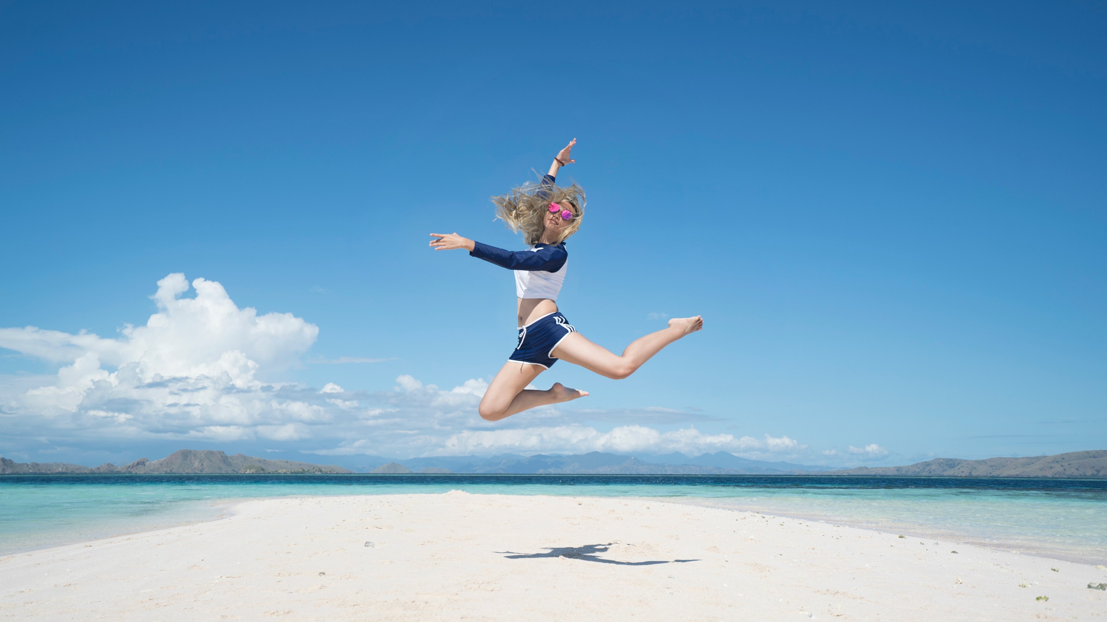 a young woman jumping high above a patch of white sand surrounded by the turquoise sea, jump for your life 4k, HD Wallpaper