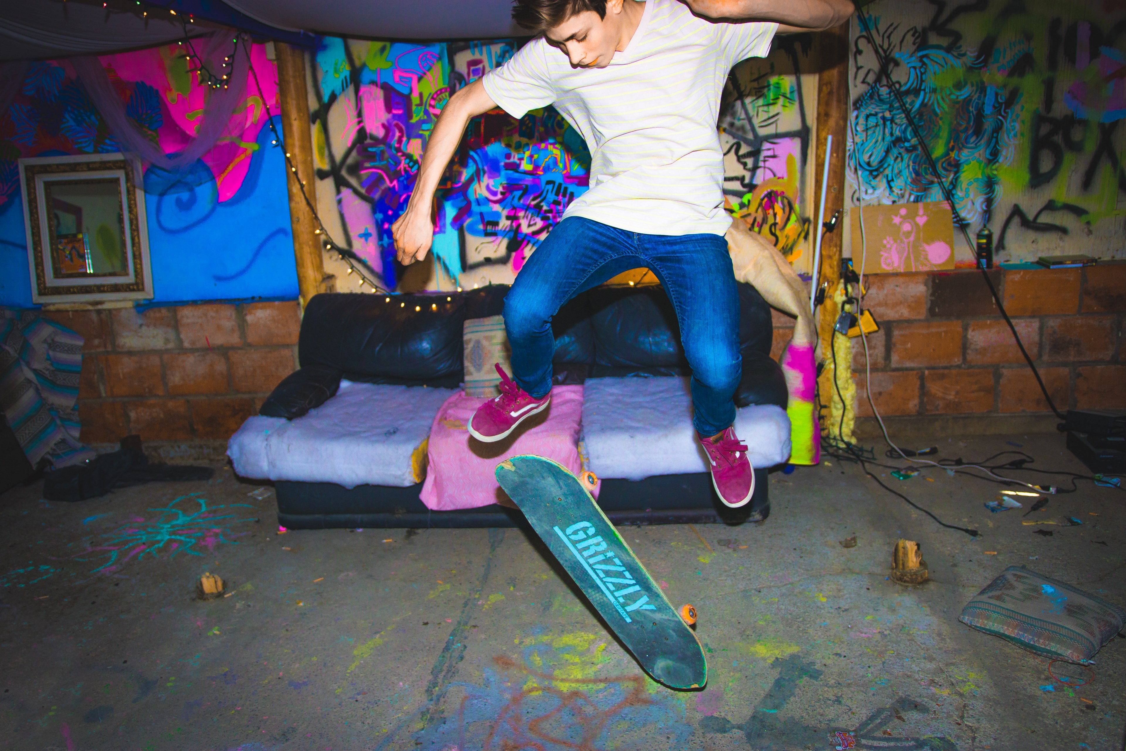 a skateboarder does a trick in front of a couch and neon graffitied wall, skateboarder in front of couch 4k, HD Wallpaper