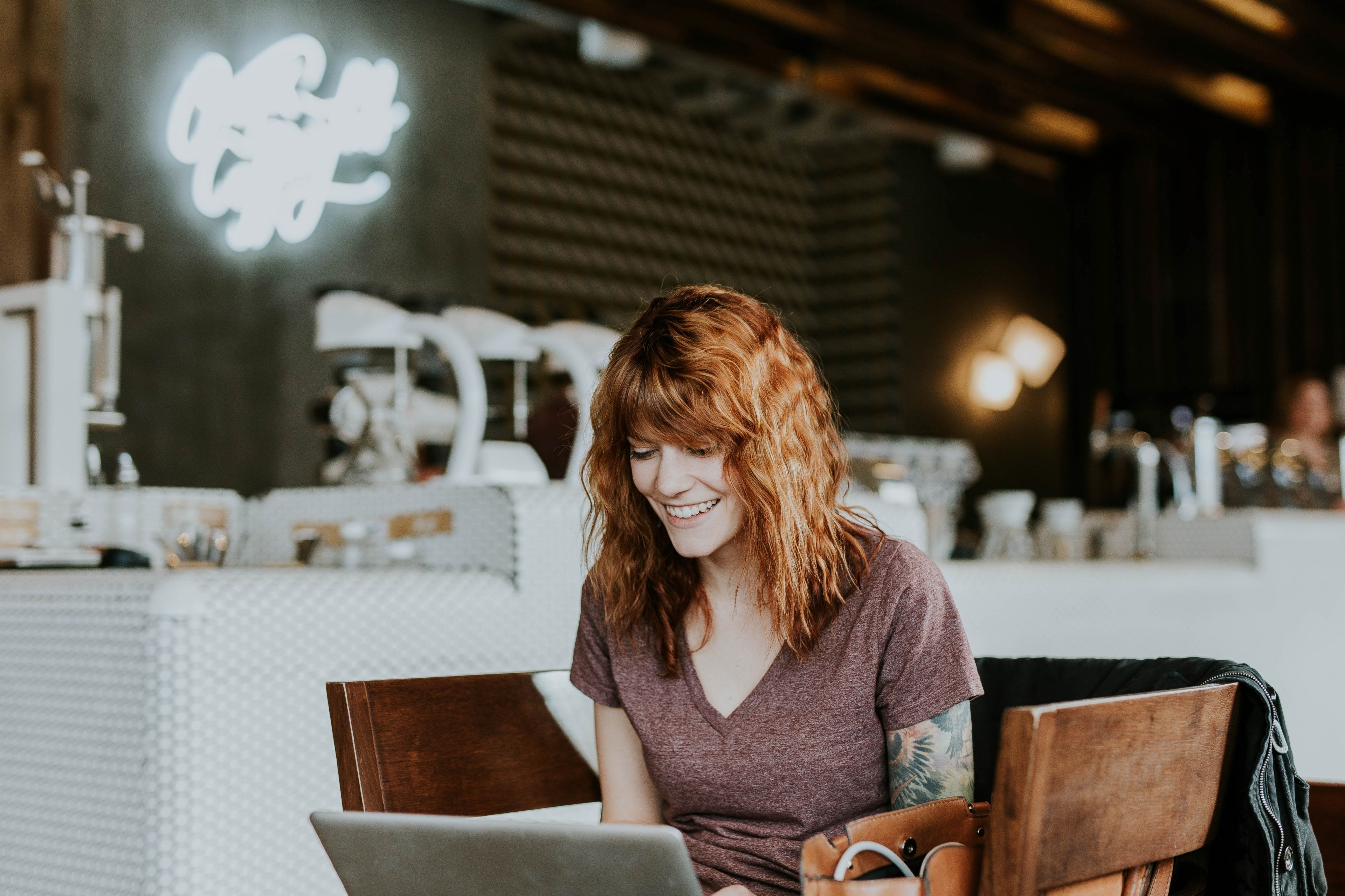 a young woman smiling while looking at a laptop screen at a coffee shop, tattooed woman with laptop 4k, HD Wallpaper