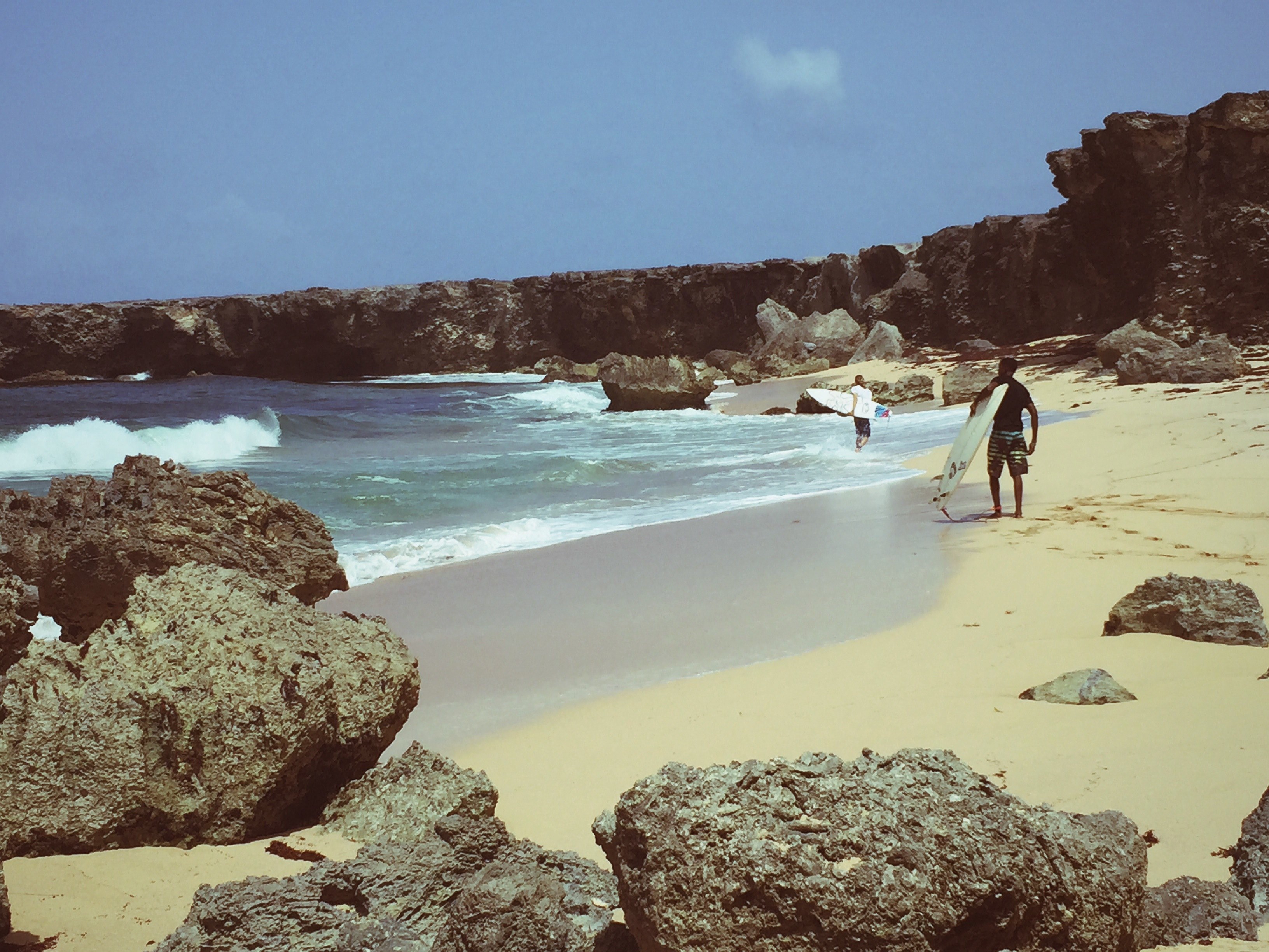 two surfers on the sand beach in bay among rocky cliffs, the perfect spot for surfing 4k, HD Wallpaper
