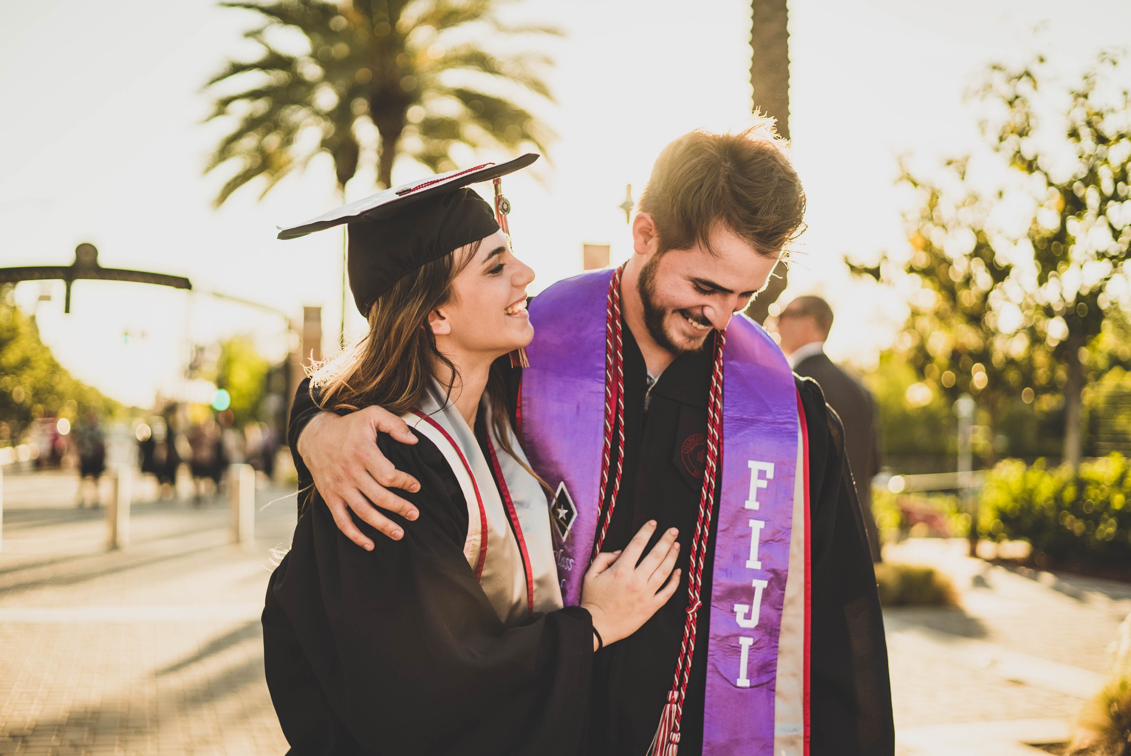 a man and woman both smiling in graduation attire the sun and palm trees behind them with bokeh effect, graduation man woman and caucasian 4k, HD Wallpaper