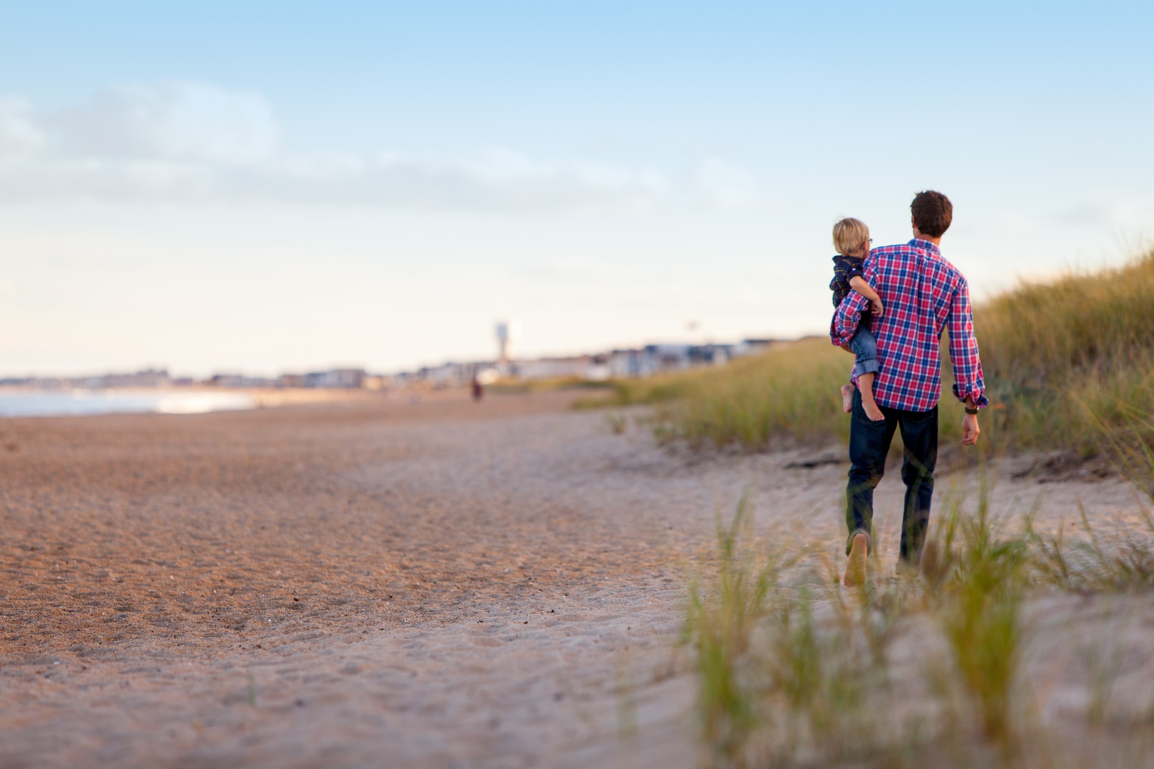 father in plaid shirt and jeans holds child on hip as they walk along the dunes, among the dunes 4k, HD Wallpaper