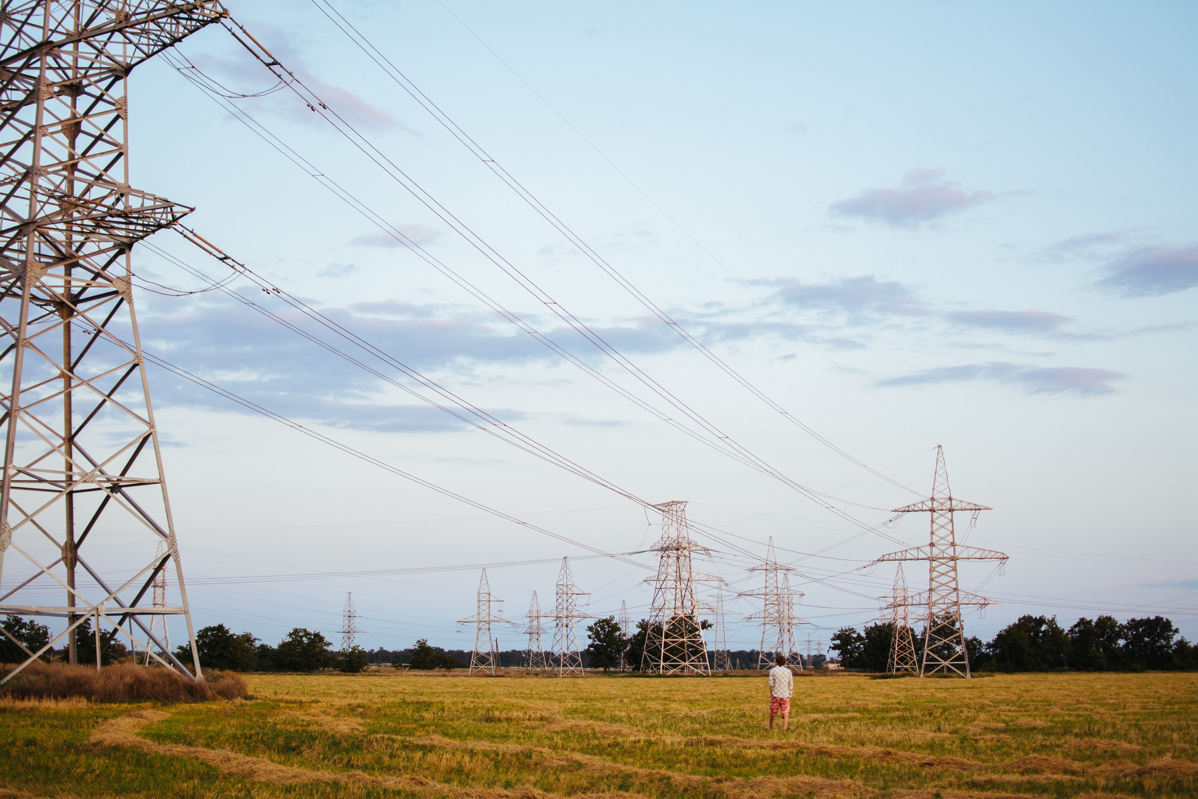 man in a white shirt and red shorts standing in a field gazing at the pylons and power lines running between them under a slightly cloudy sky, powerlines in the pasture 4k, HD Wallpaper