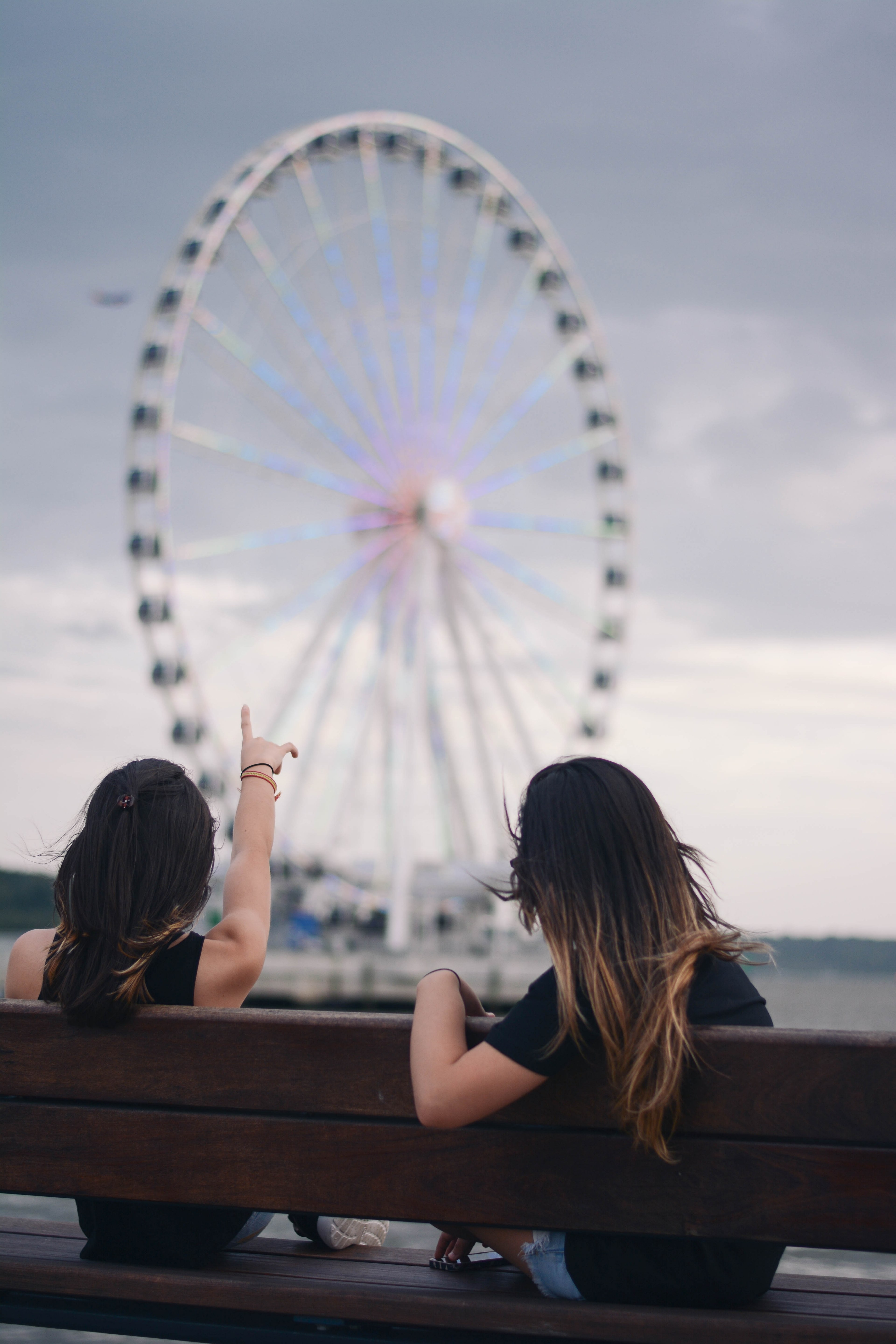 women sitting on wooden bench looking and pointing at the national harbor ferris wheel, women admiring ferris wheel 4k, Phone HD Wallpaper