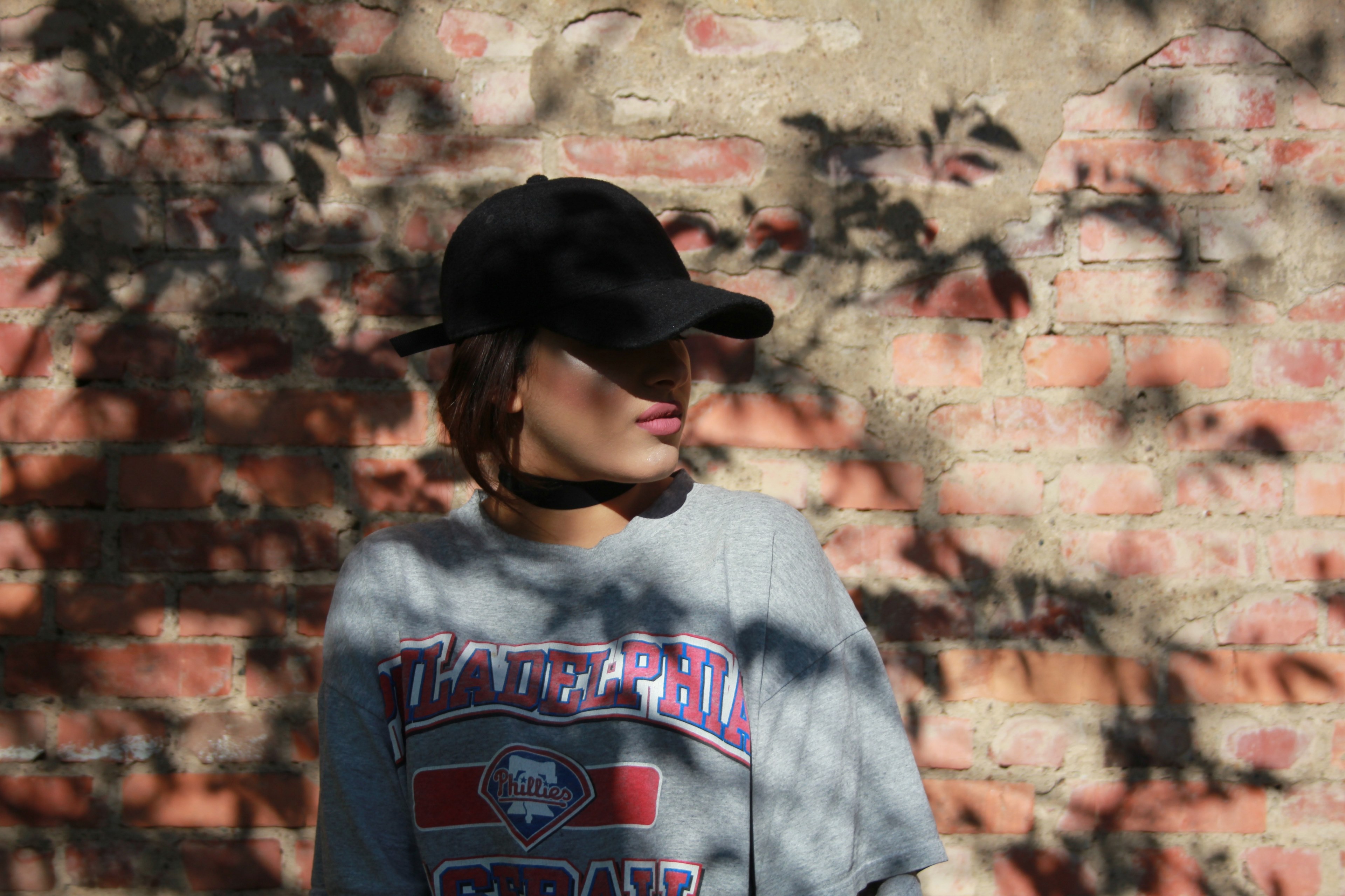 a lady wearing lipstick cap and a t shirt with logo on it standing by a brick wall, lady by brick wall 4k, HD Wallpaper