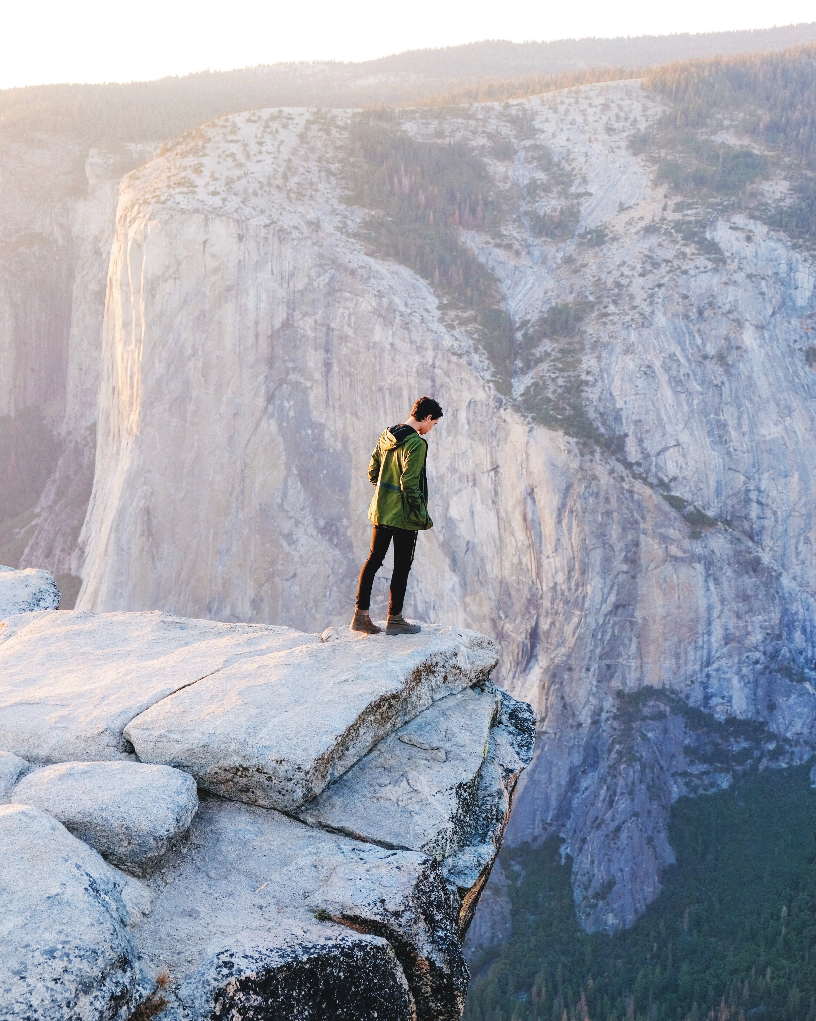 a man wearing black pants and a green jacket leaning over the edge of a cliff in yosemite valley, yosemite valley cliff 4k, Phone HD Wallpaper