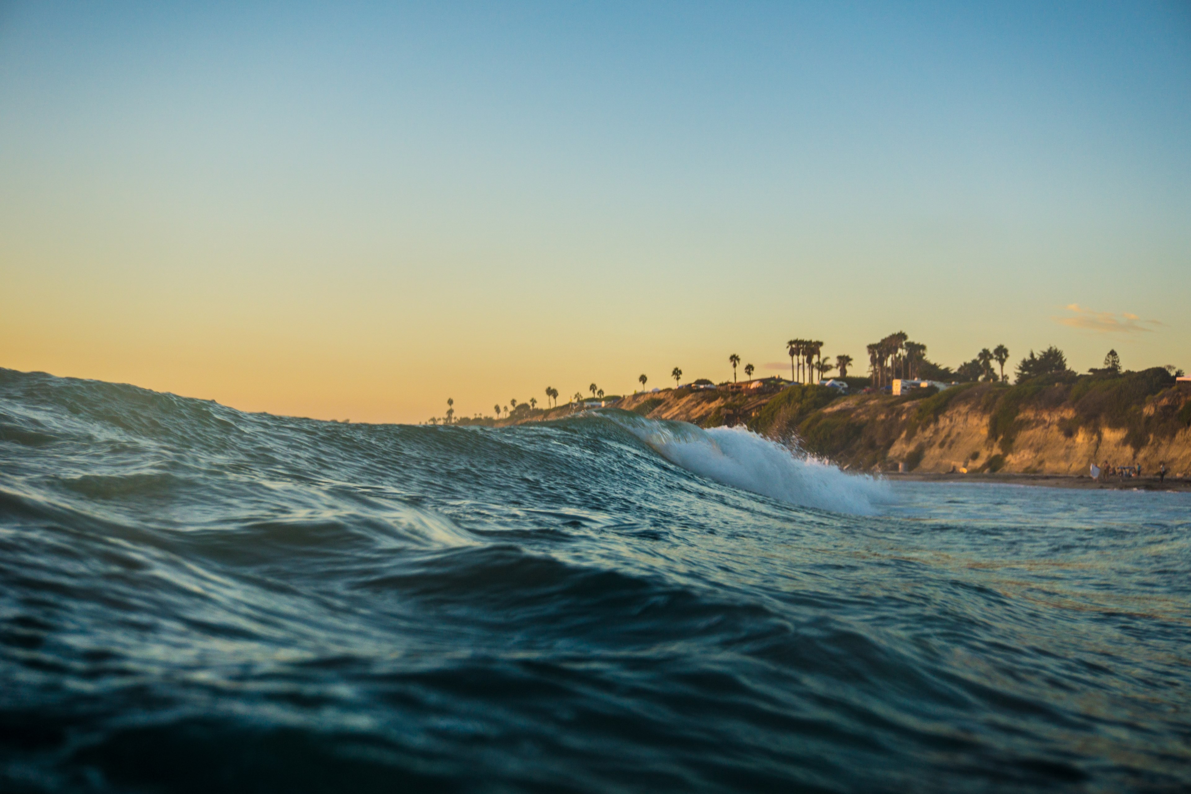 a wavy sea beneath a sunset with coastal cliffs and trees in the distance, ocean waves on a beach 4k, HD Wallpaper
