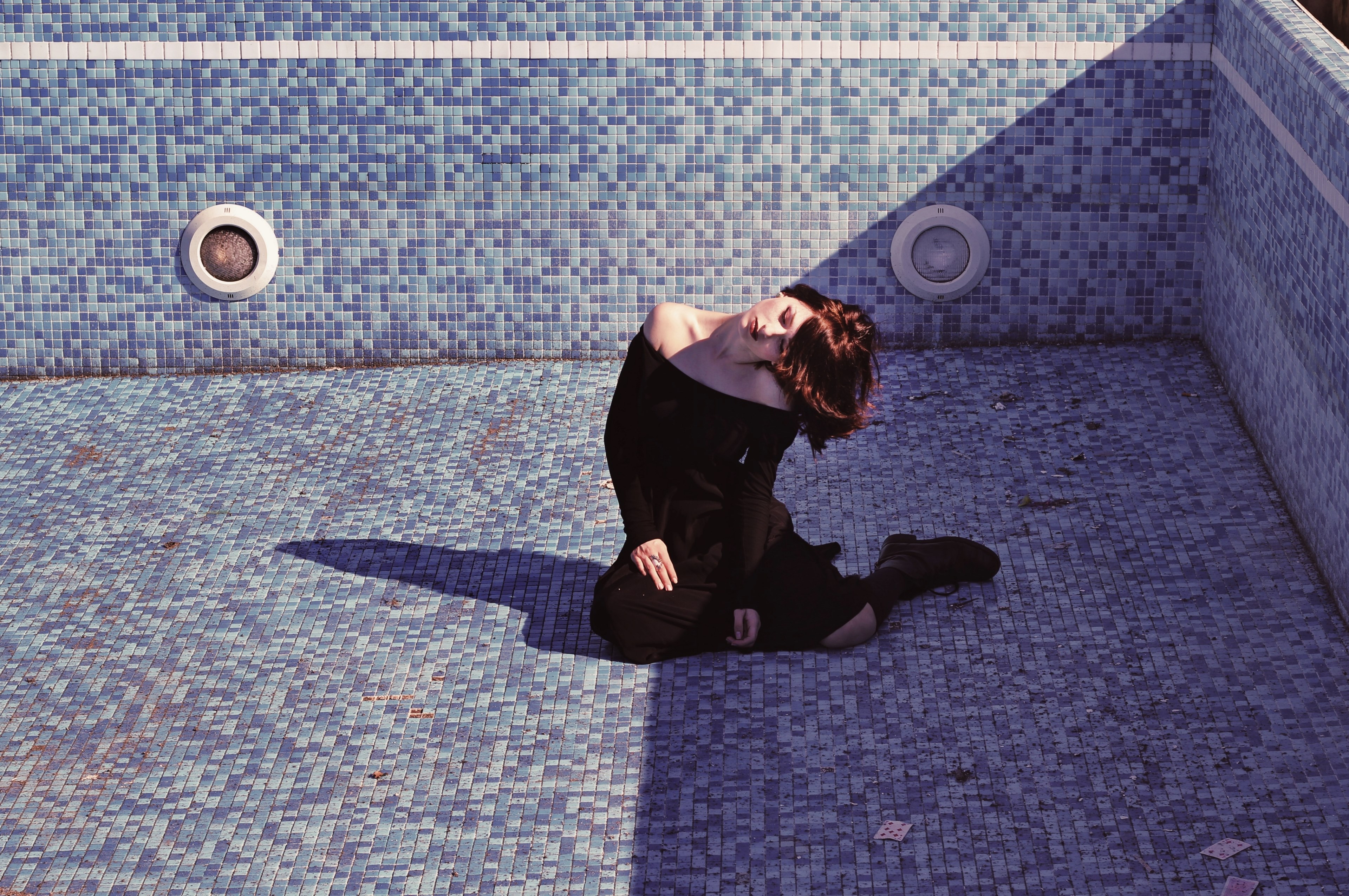 a woman sits tilting her head to the side on the bottom of an empty pool, woman in empty pool 4k, HD Wallpaper