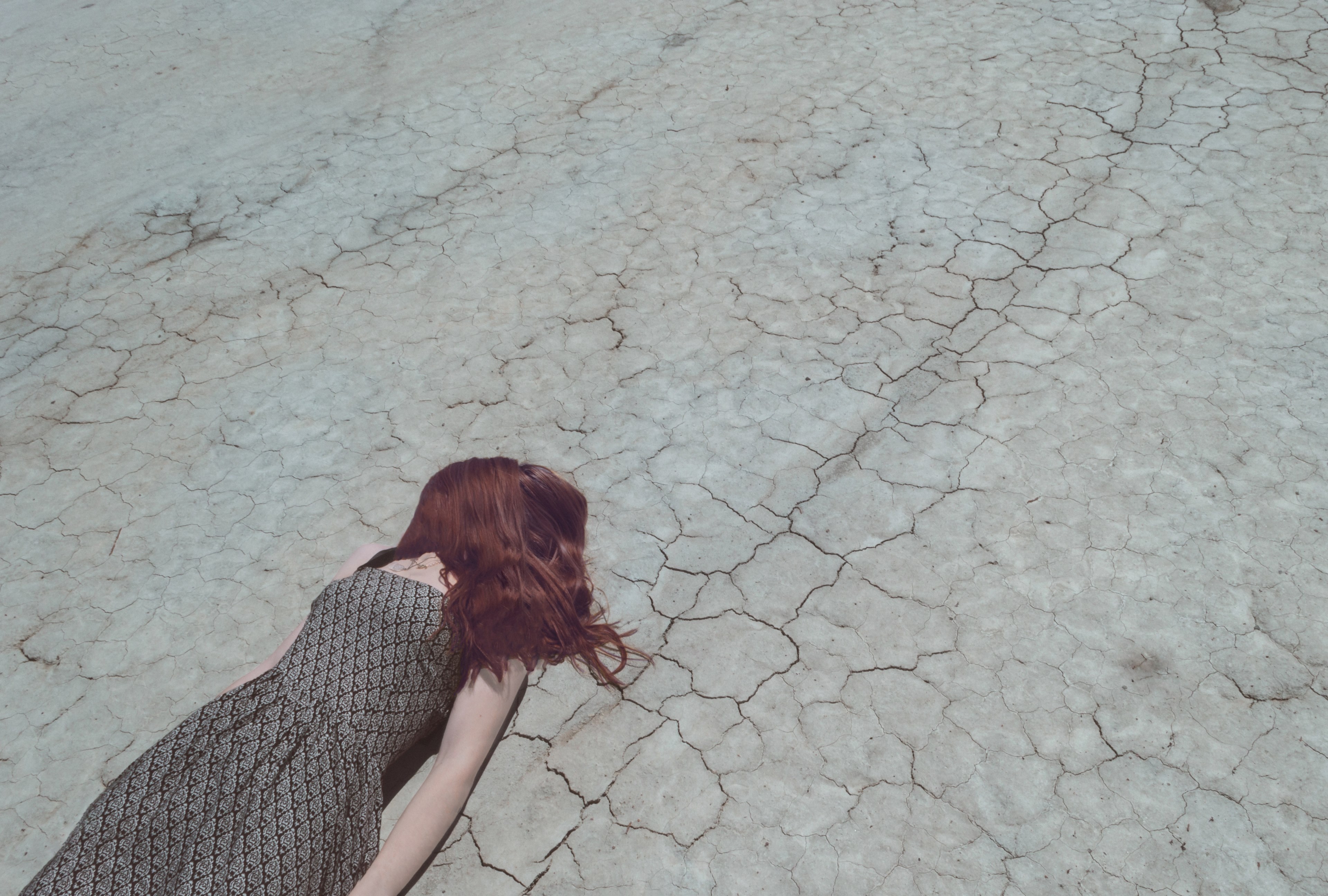 woman with hair over face lying down on cracked desert floor, exhausted from the heat 4k, HD Wallpaper