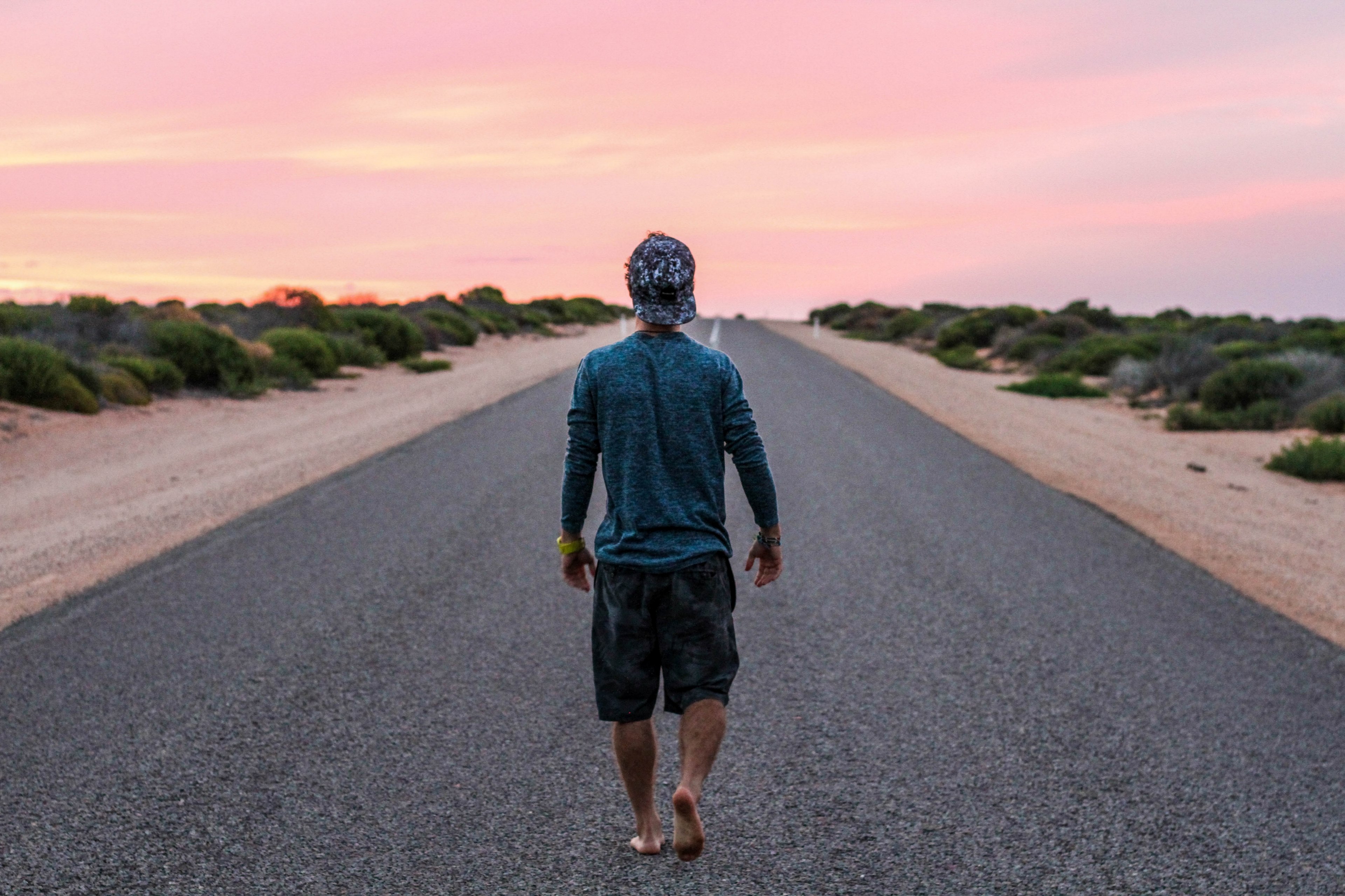 a barefoot man in a baseball hat walking on an empty asphalt road during sunset, lone man on an asphalt road 4k, HD Wallpaper