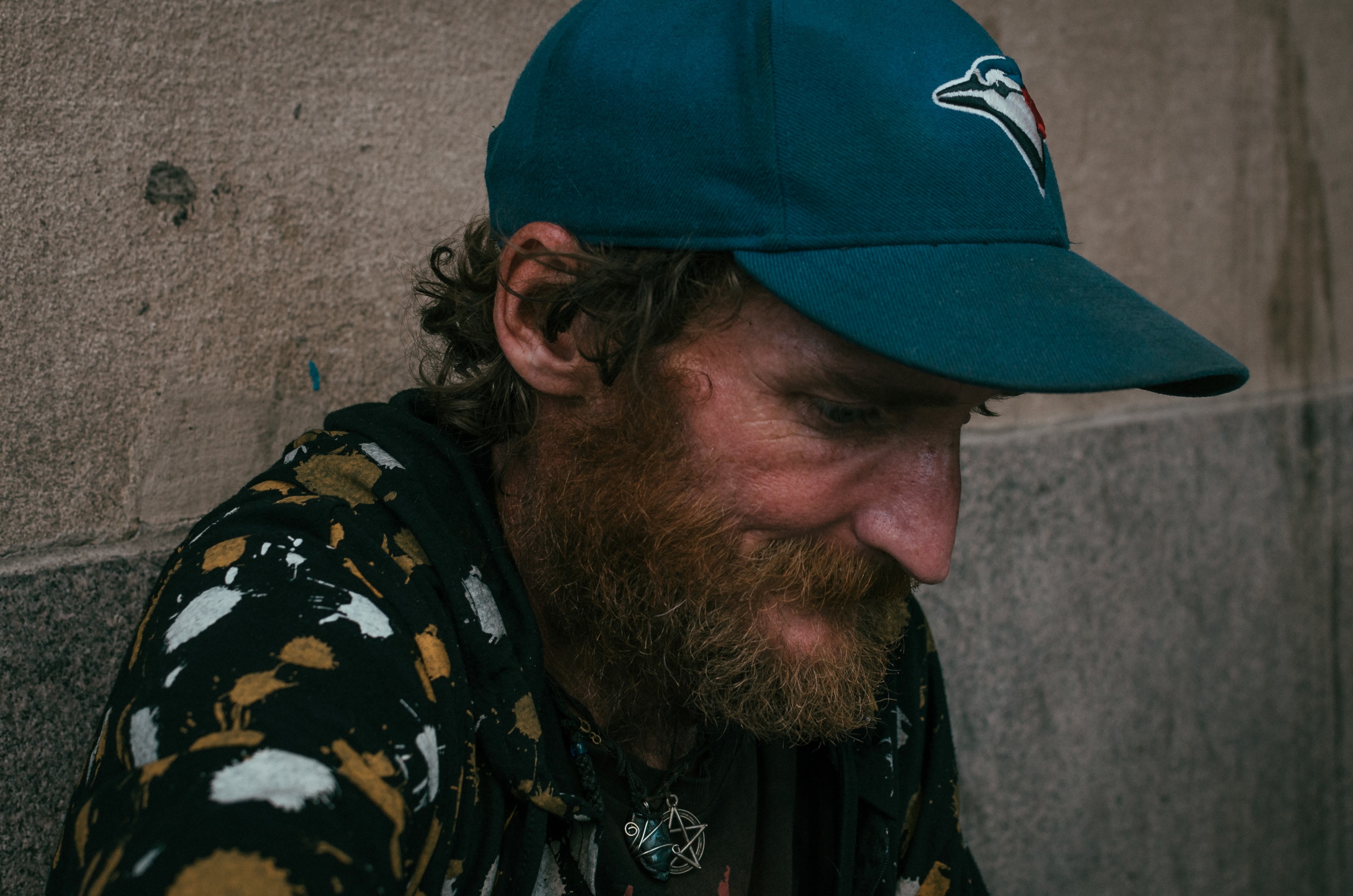 a bearded man wearing a blue jays cap and a pentagram pendant looks down while sitting, _the streets 2 4k, HD Wallpaper