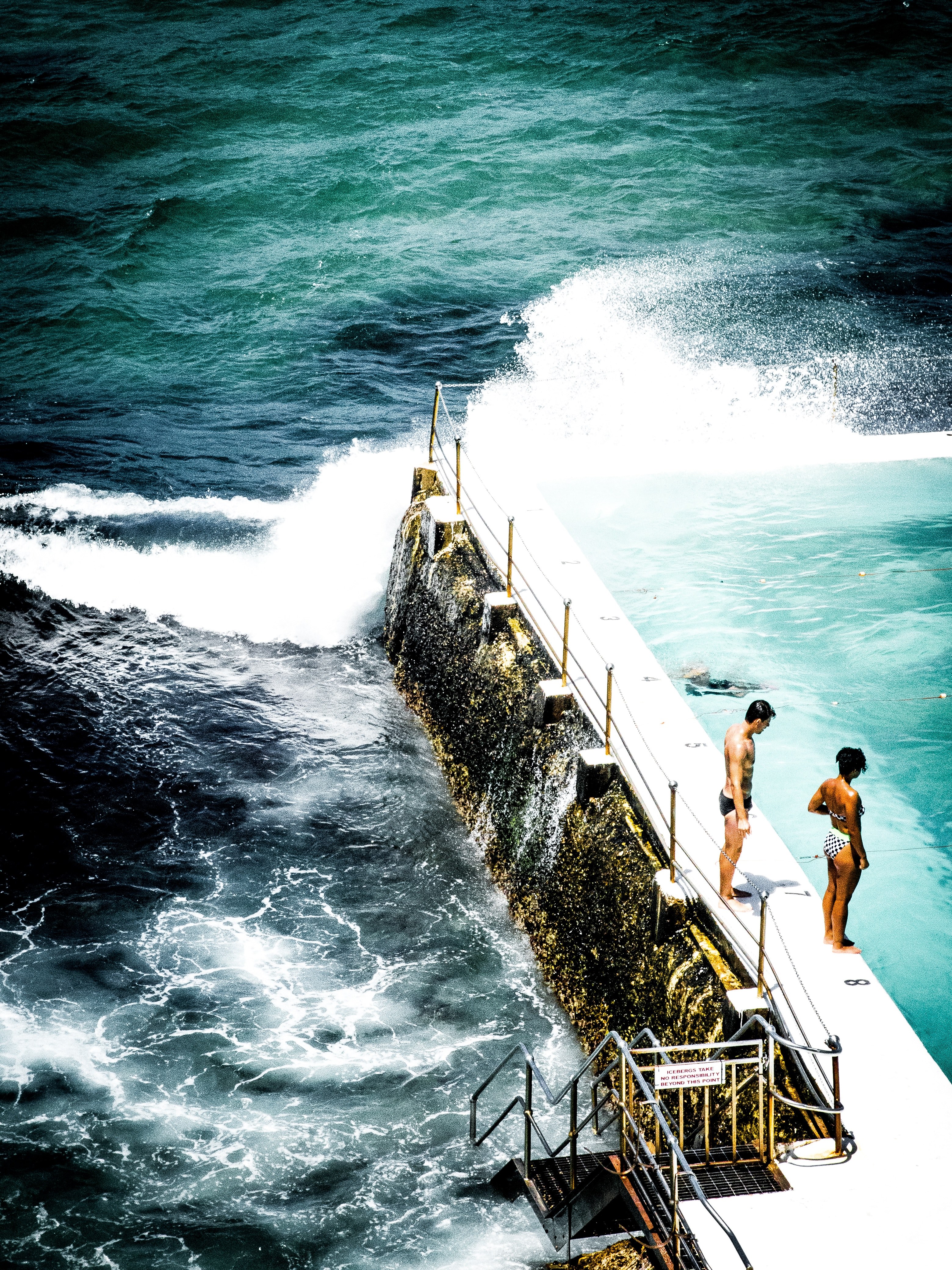 a couple standing on the step of an outdoor pool to swim in bondi icebergs pool, a couple standing by pool step 4k, Phone HD Wallpaper