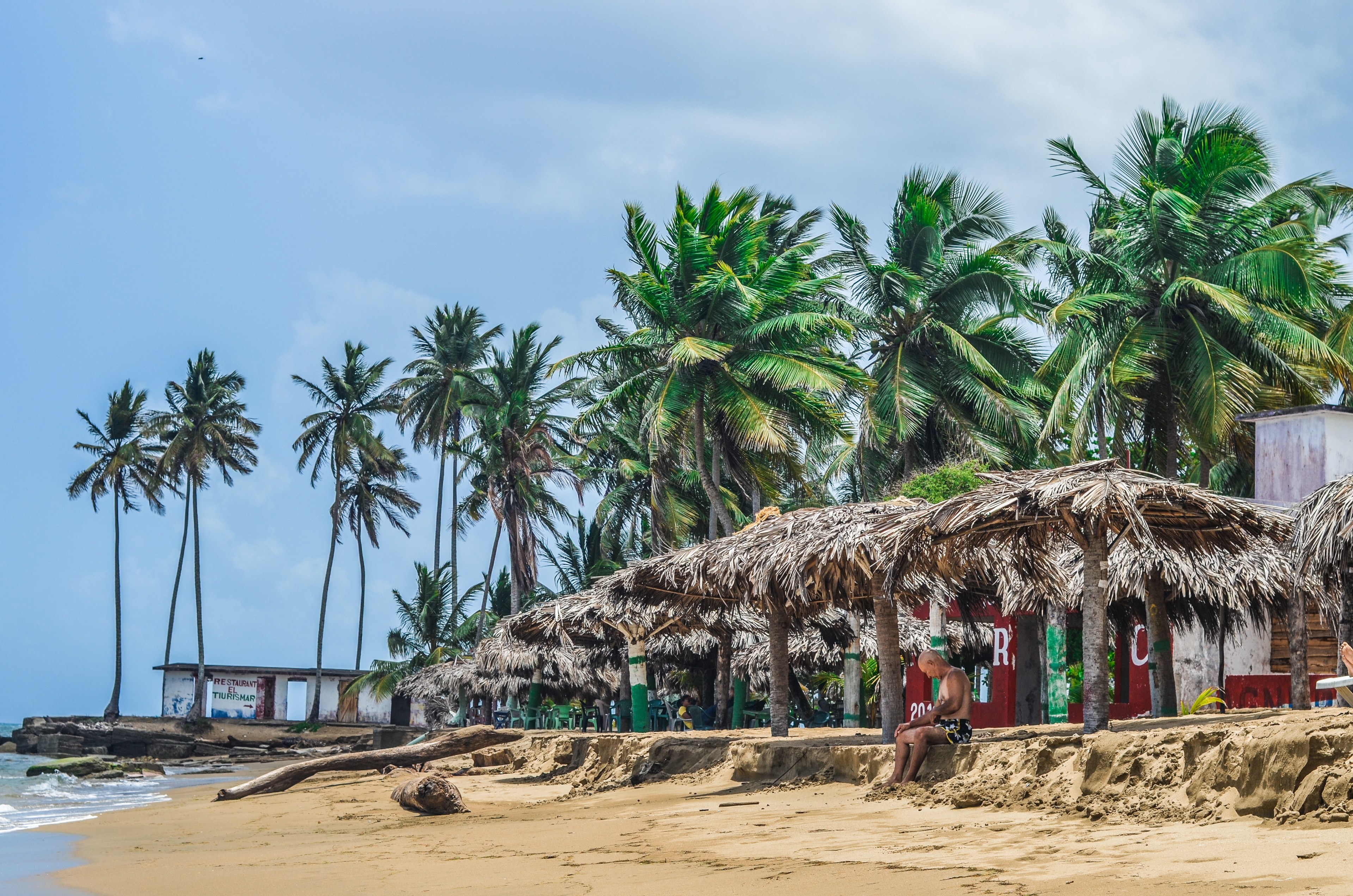 a lone man sitting on the beach under a thatched roof, sheltering from sun on a beach 4k, HD Wallpaper