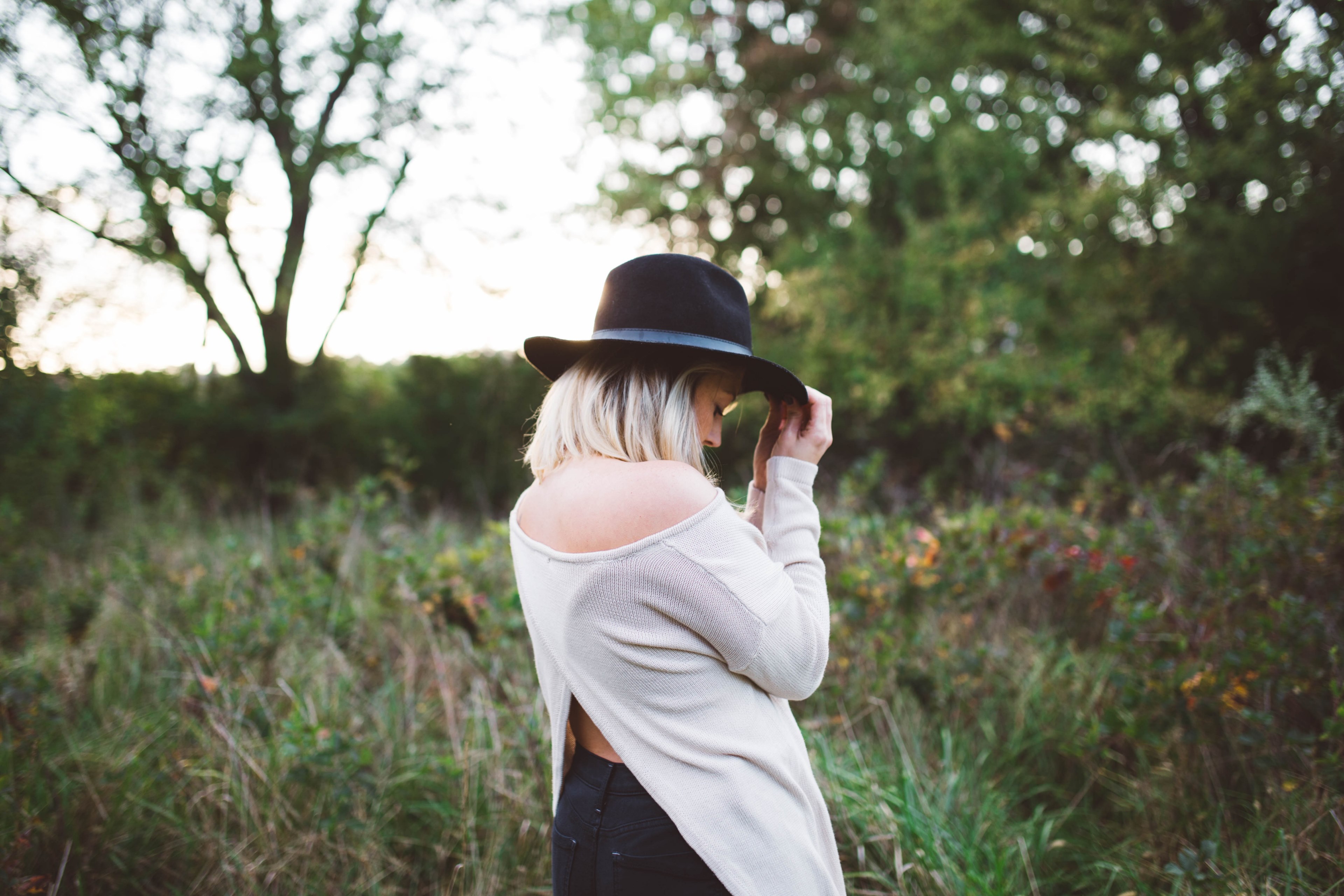 a blonde woman holding the brim of her black hat in a meadow, woman in black hat on a meadow 4k, HD Wallpaper