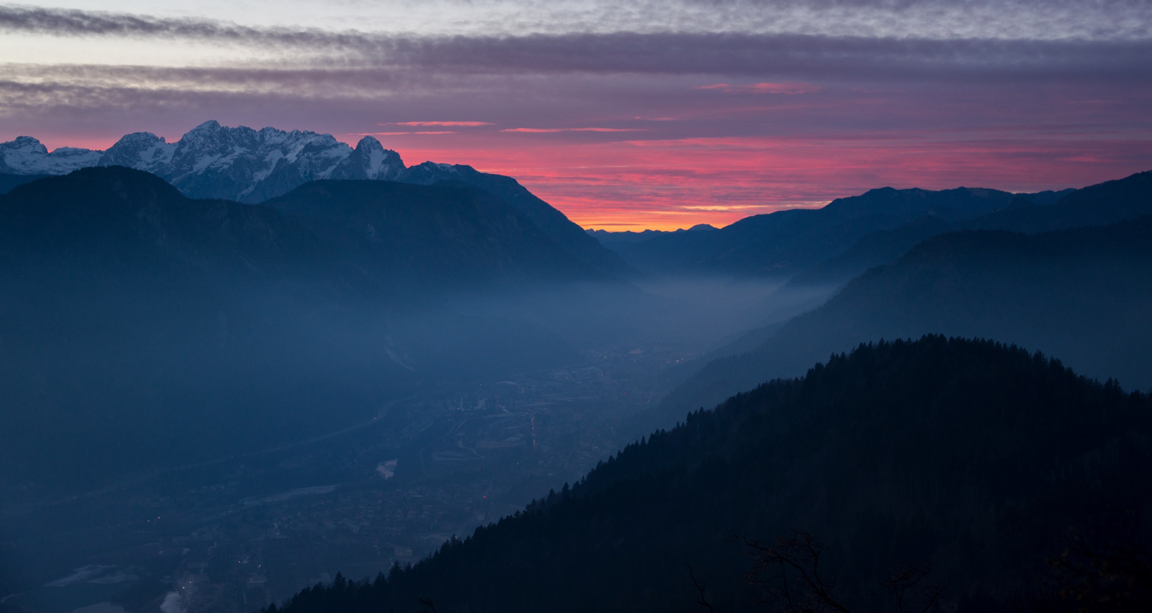 an aerial view in ajdna as a mist settles into the valley_ the sunrise or sunset behind the distant snowcap mountains turn the cloudy sky orange and pink, dark sunset 4k, HD Wallpaper