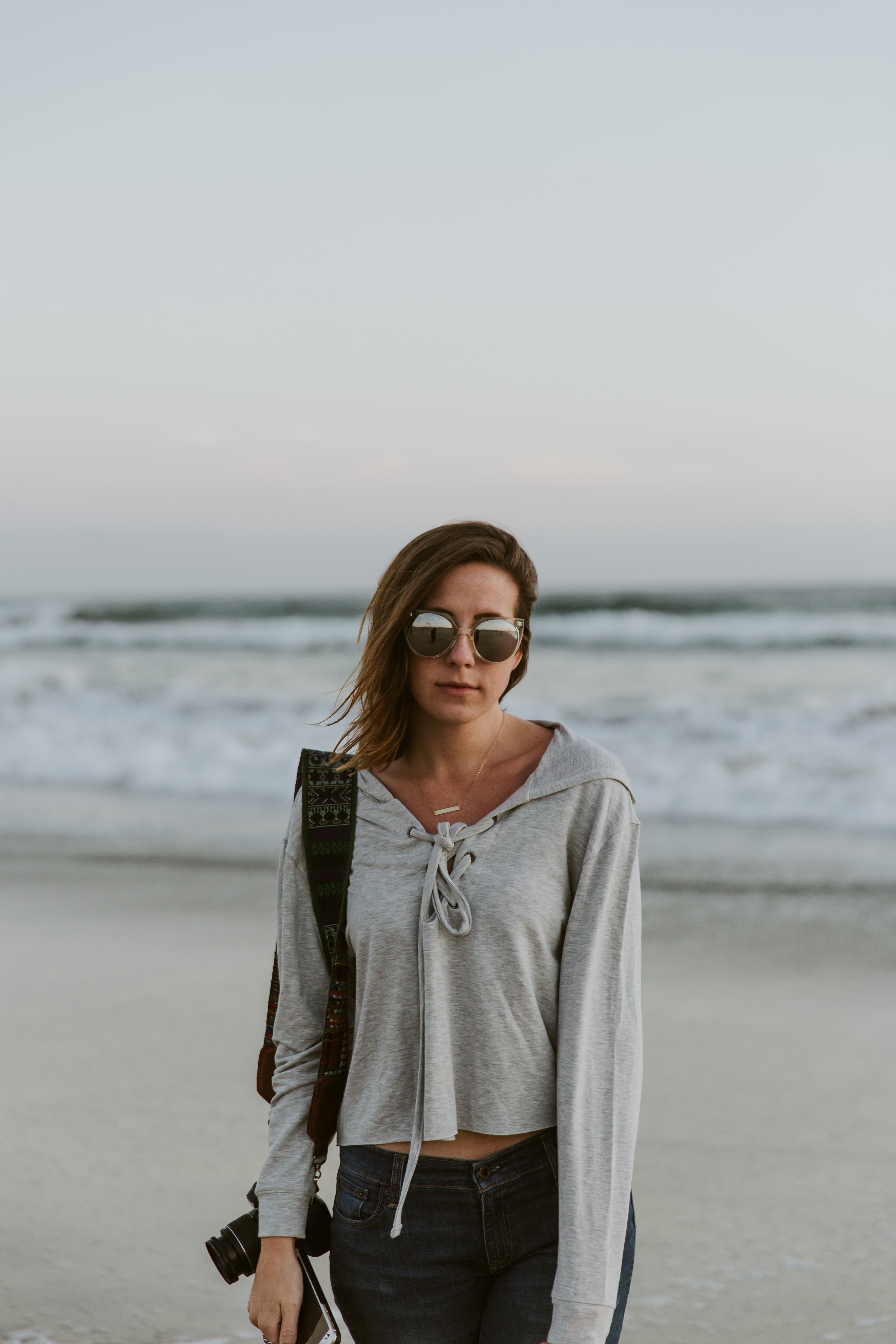 woman in sweatshirt and sunglasses holding a camera and phone with her back to the beach, woman with a camera on the beach 4k, Phone HD Wallpaper