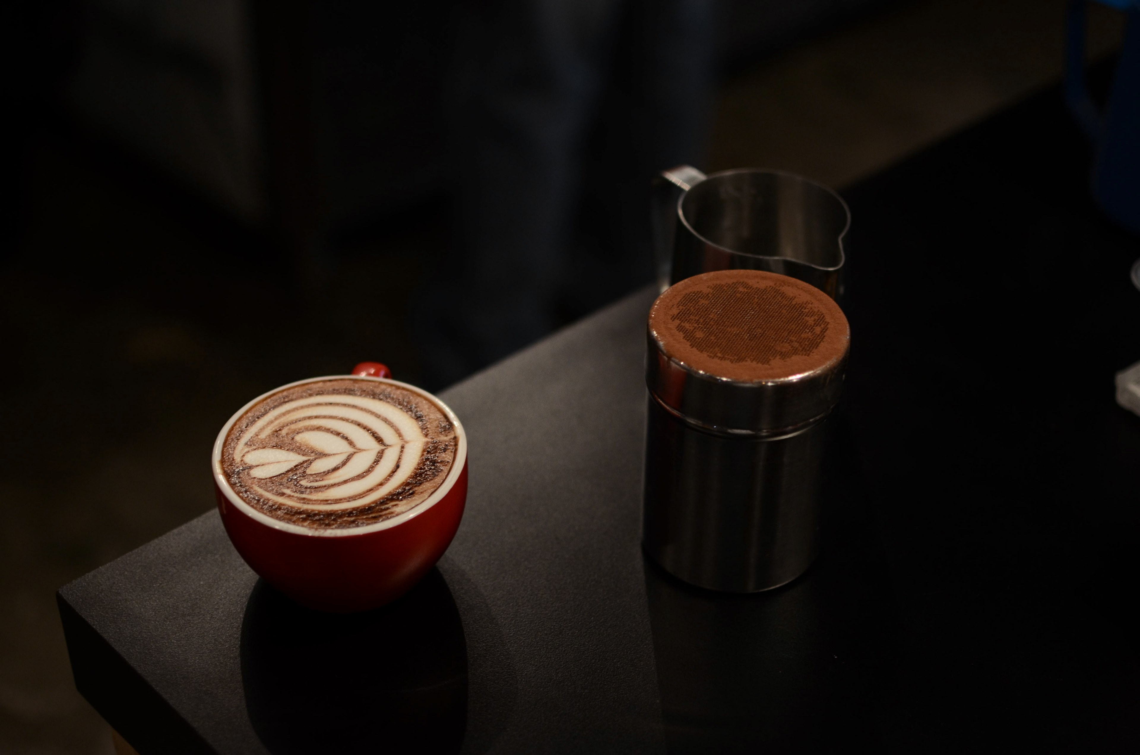 cappuccino in a red mug with leaf like foam art and two tin cream and sugar containers next to it on a wooden table, coffee with cream and sugar 4k, HD Wallpaper
