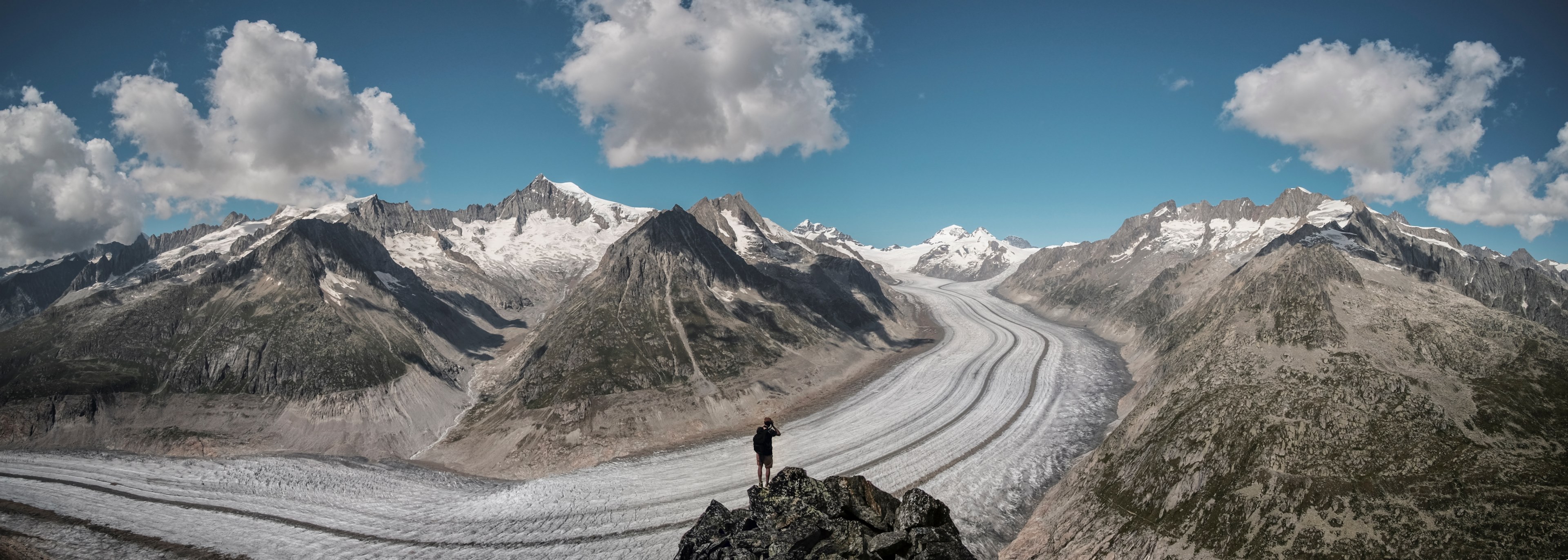 a lone man standing on a rock outcropping on the side of a snowy road up the mountains, climbing up the snowy mountain road 4k, HD Wallpaper