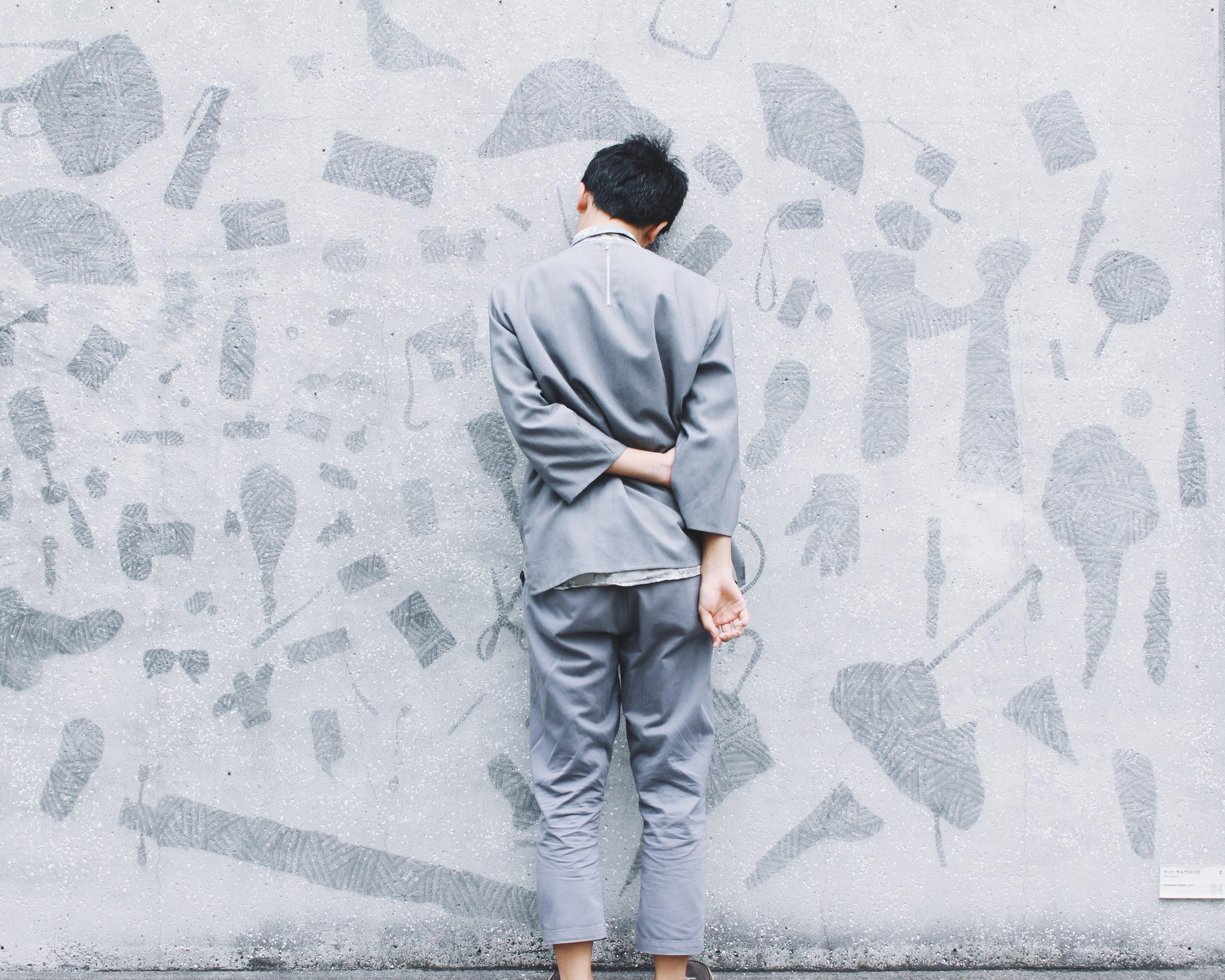 man wearing gray suit leans face first against gray wall with art, man leans against gray wall 4k, HD Wallpaper