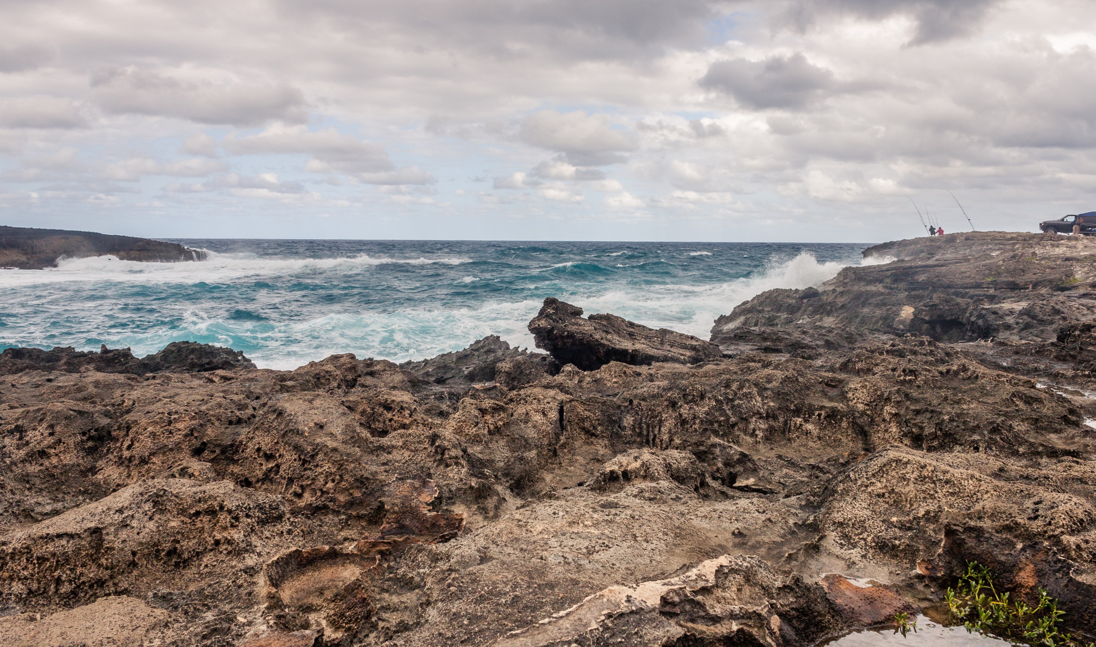 azure waves crash against the rocky shore as two silhouettes sit with fishing rods in the distance, fishing on the rocky shore 4k, HD Wallpaper
